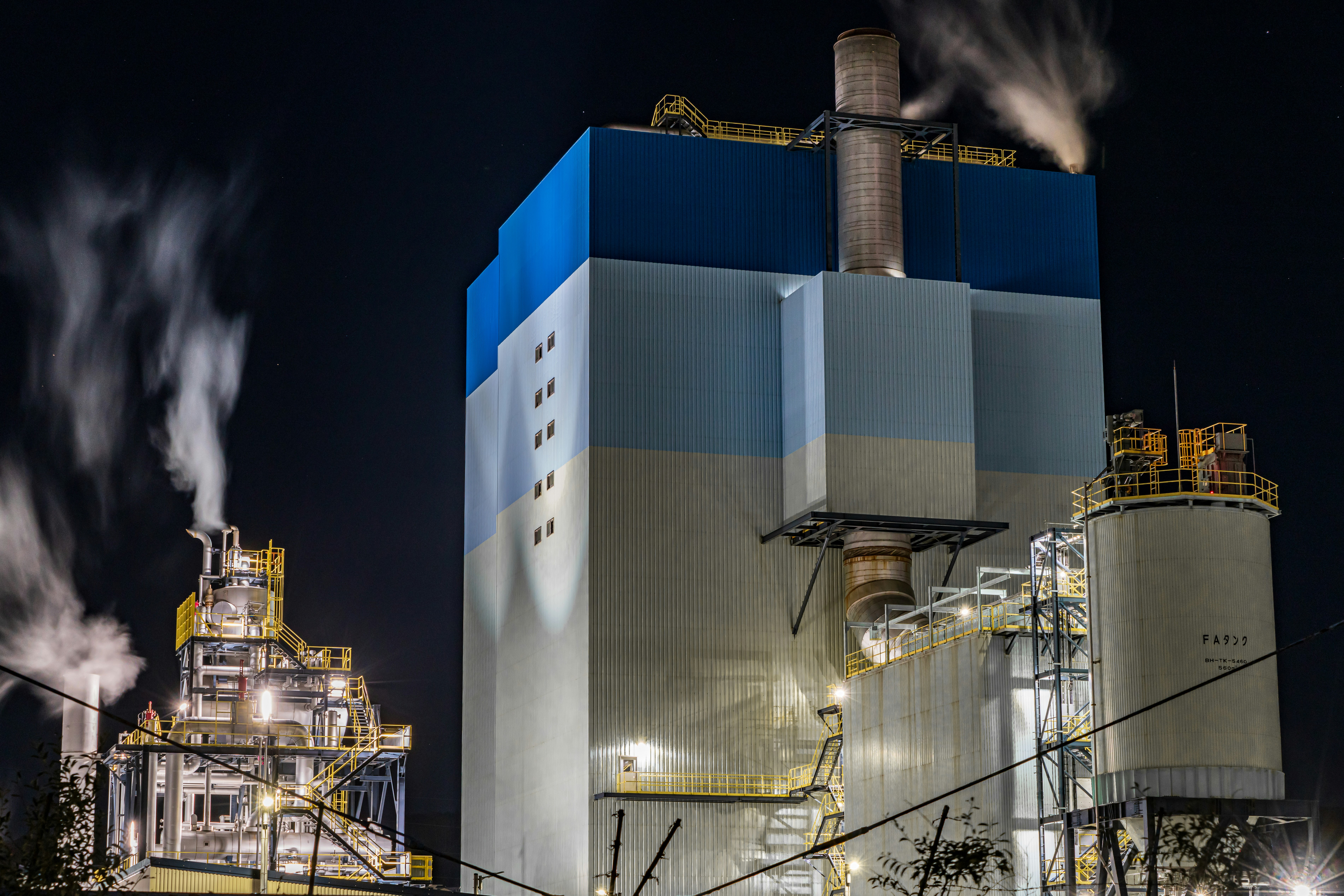 night industrial plant with smokestacks releasing steam and smoke