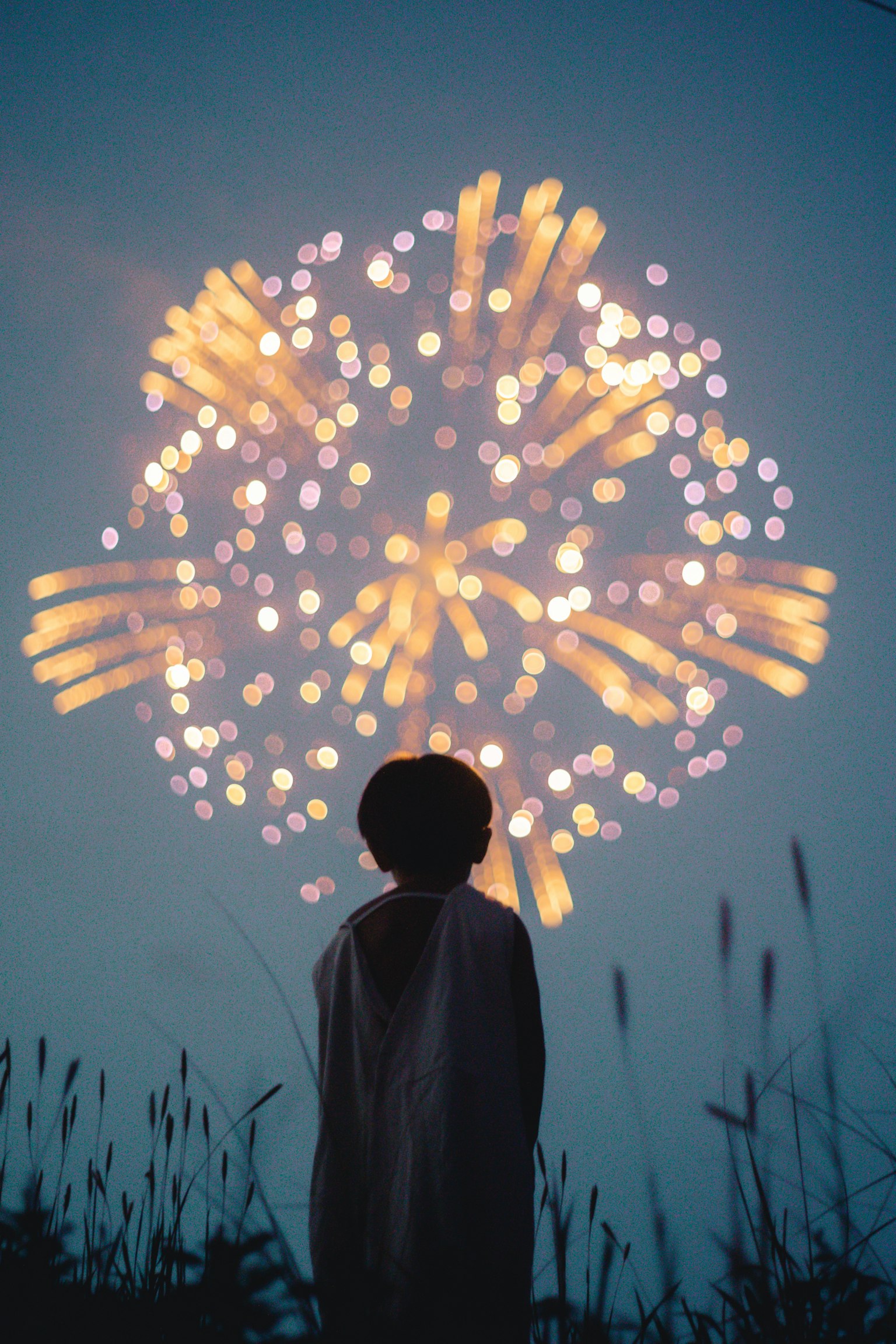Silhouette di un bambino che guarda i fuochi d'artificio colorati nel cielo notturno