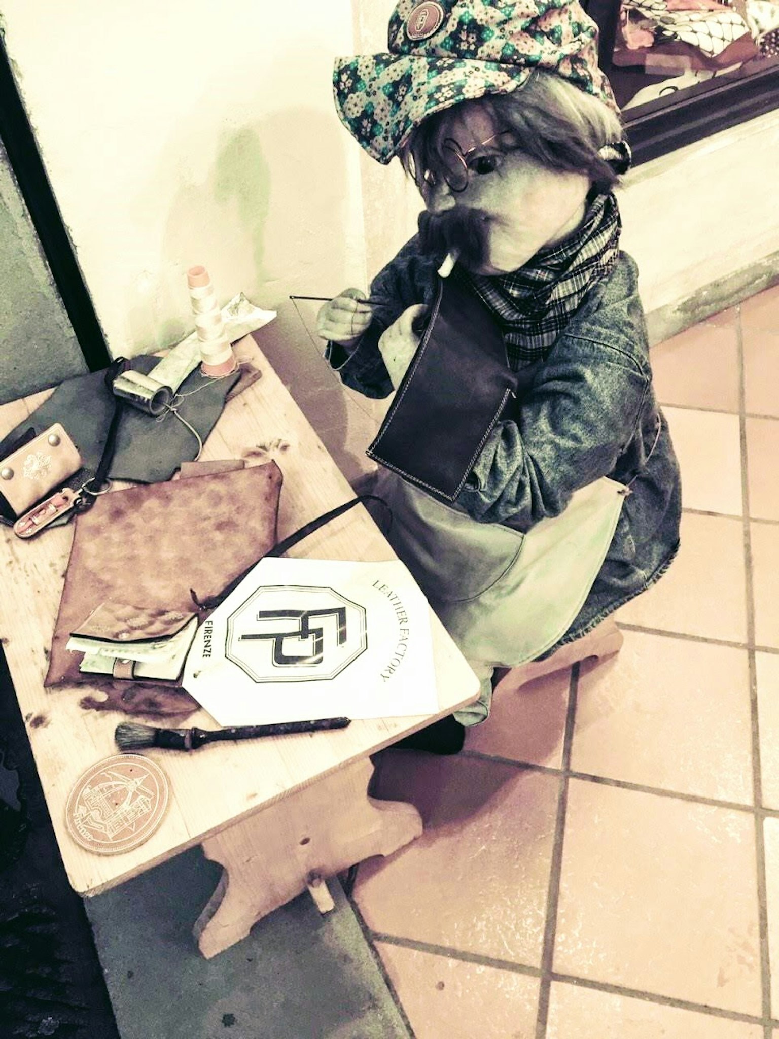 Una muñeca de niño sentada en una mesa dibujando con un sombrero peculiar y una bufanda