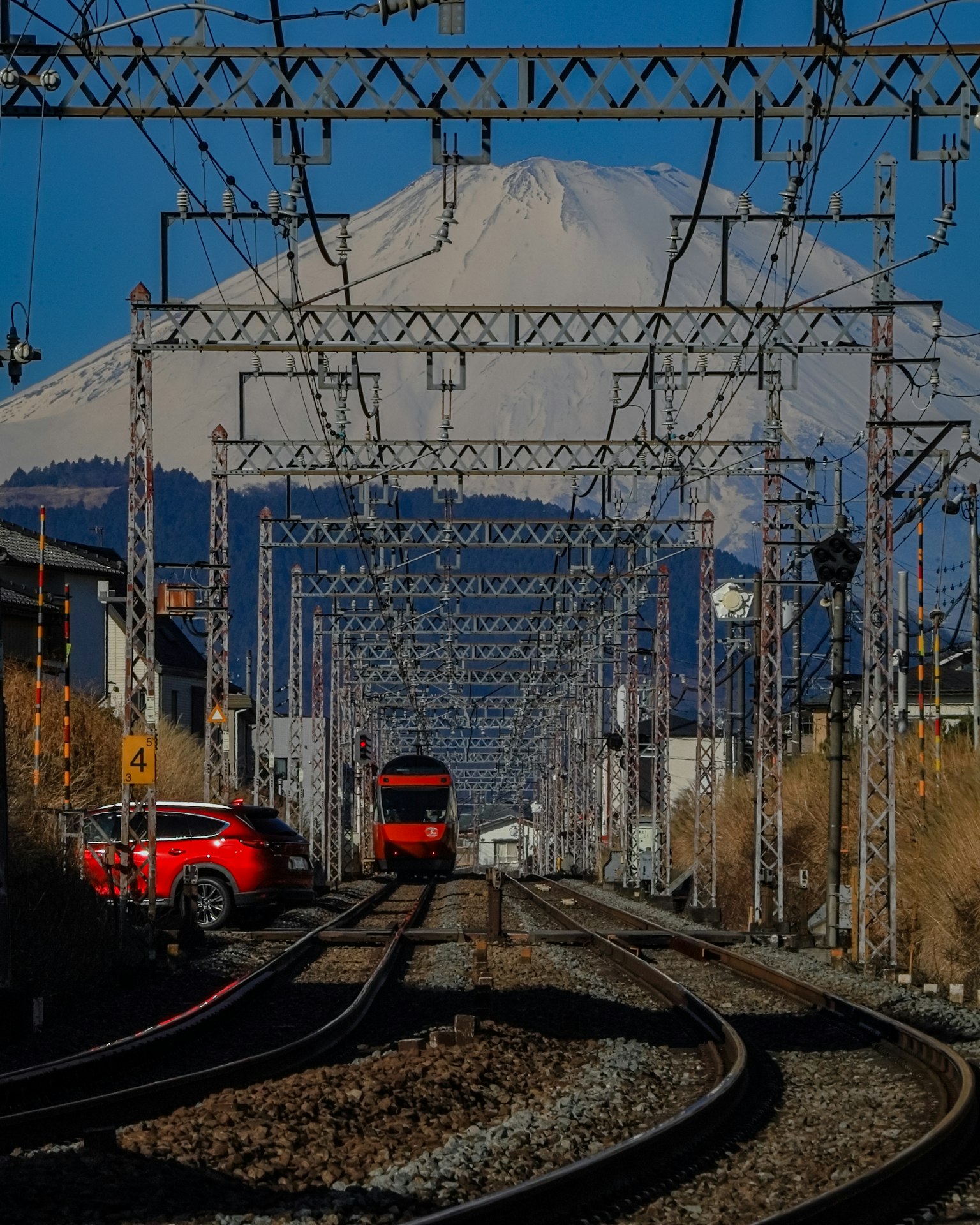 รางรถไฟที่มีรถไฟสีแดงอยู่ใต้ภูเขาฟูจิท้องฟ้าสีฟ้าใส