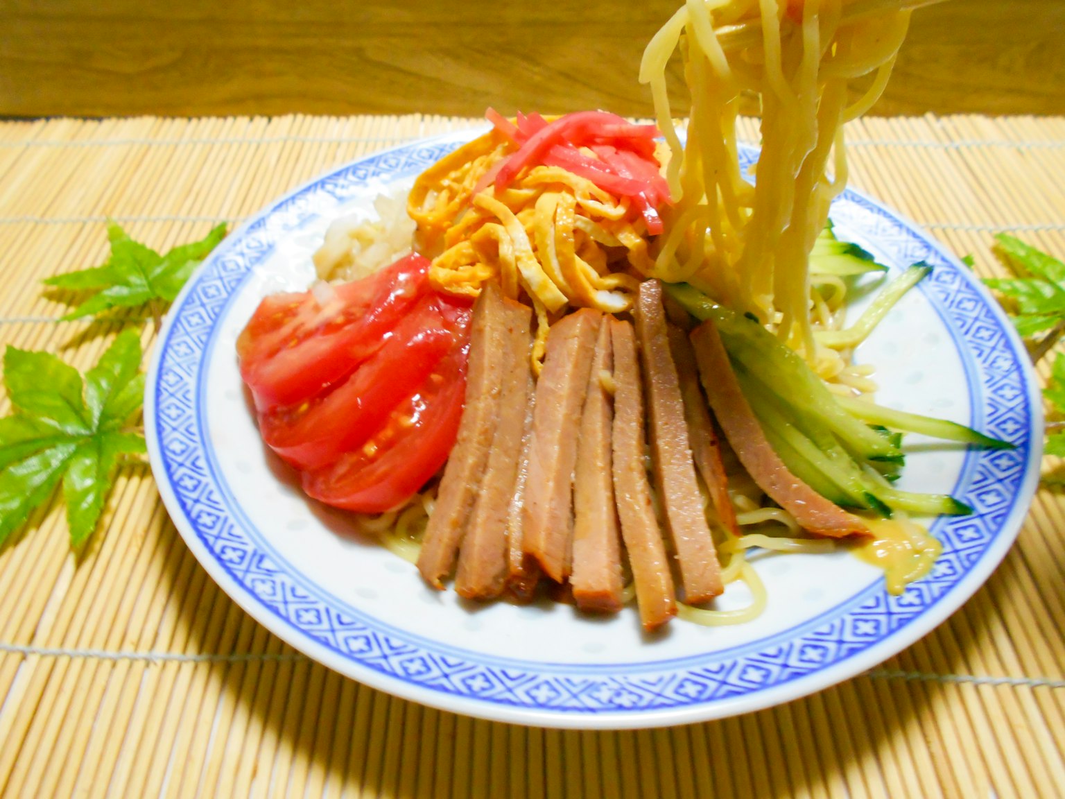 Bunt angerichteter Teller mit kalten chinesischen Nudeln, belegt mit Tomaten und Gemüse