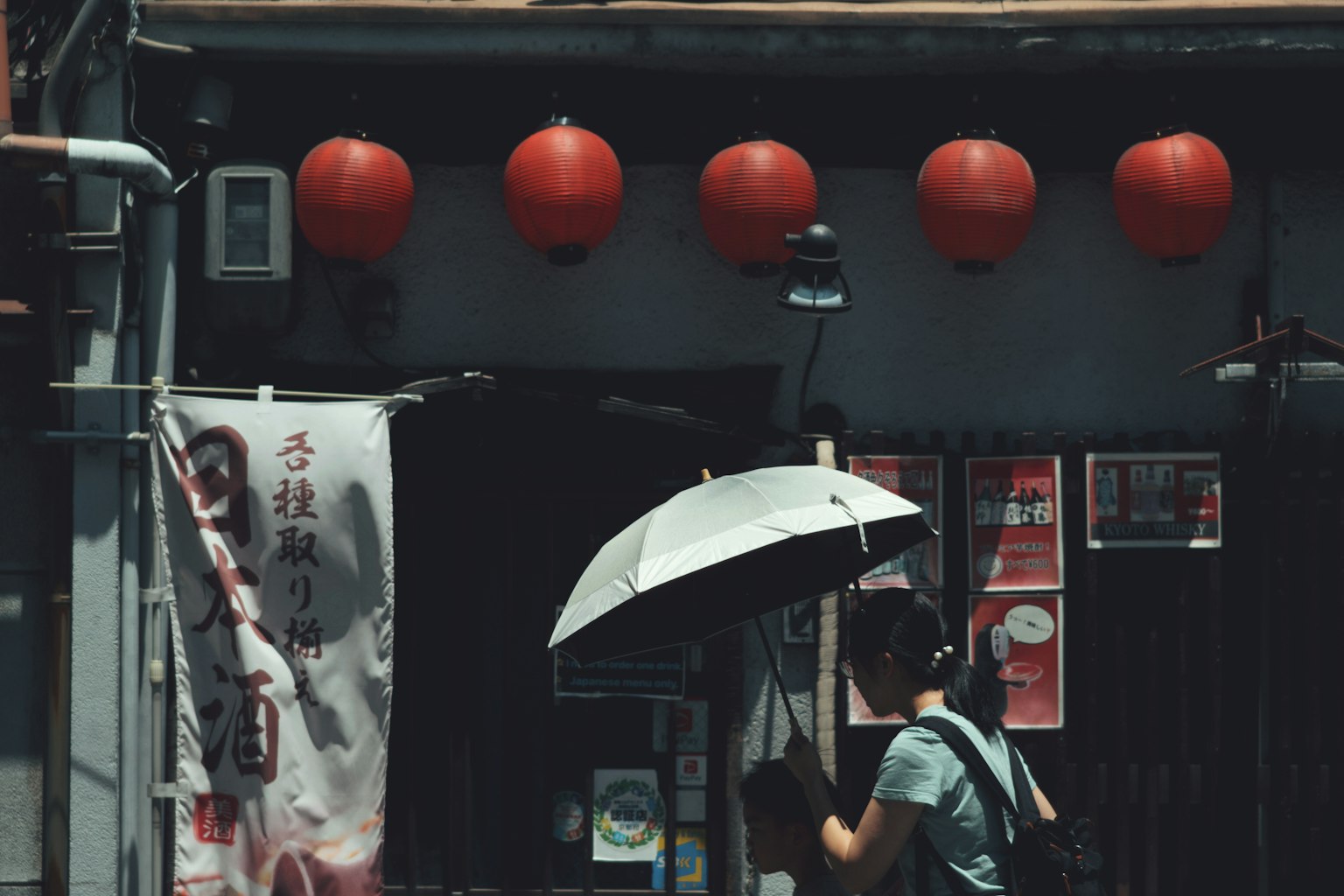 Une femme marchant avec un parapluie devant un magasin orné de lanternes rouges