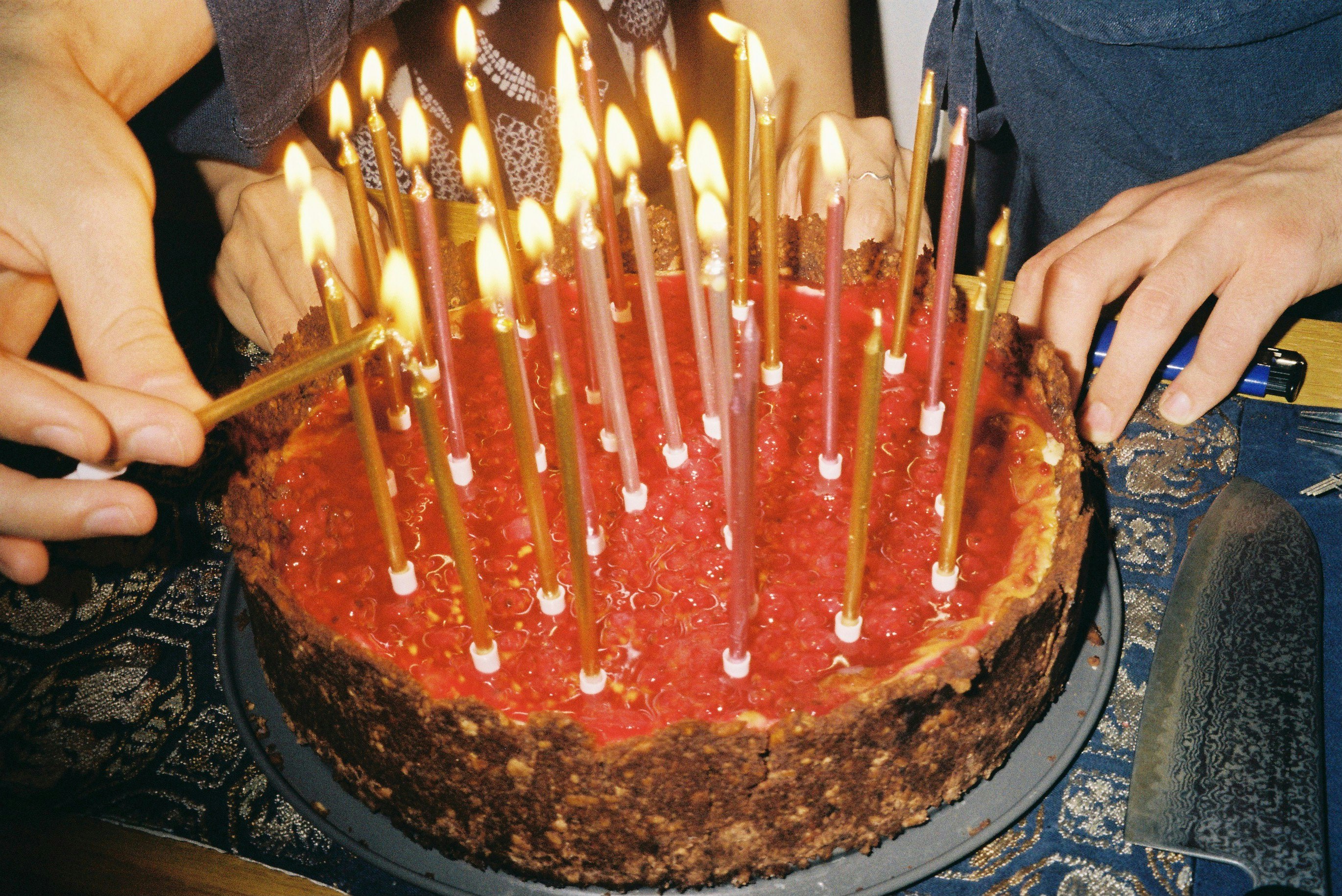 ろうそくの立つケーキを囲む手と家族の誕生日の場面