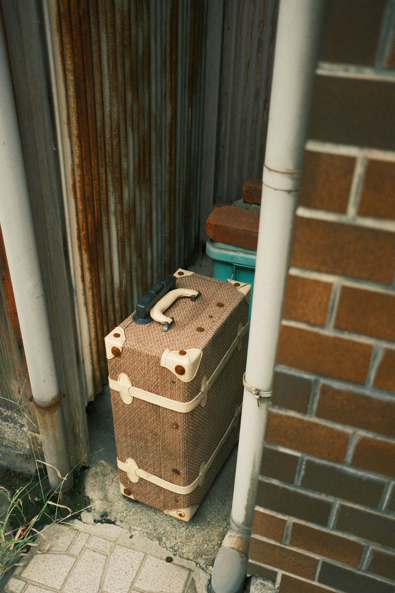 狭い通路に置かれた茶色のスーツケースと周囲のパイプ