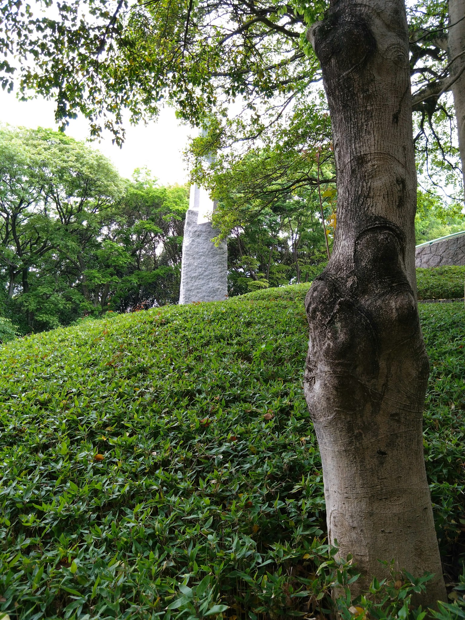 Scultura in pietra vicino a una collina verde e a un albero