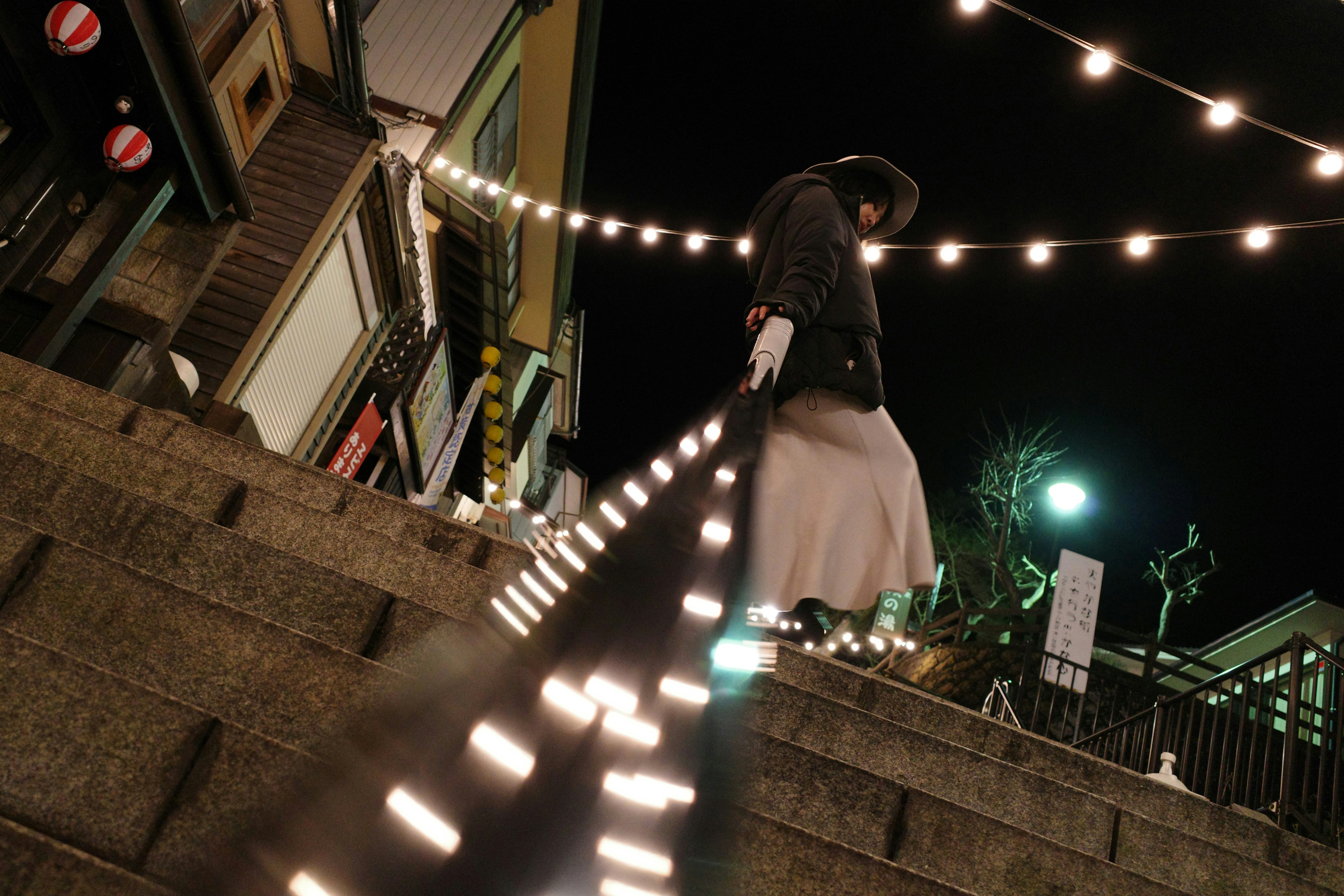 夜の階段を歩く人物と街灯の光が連なる路地の風景