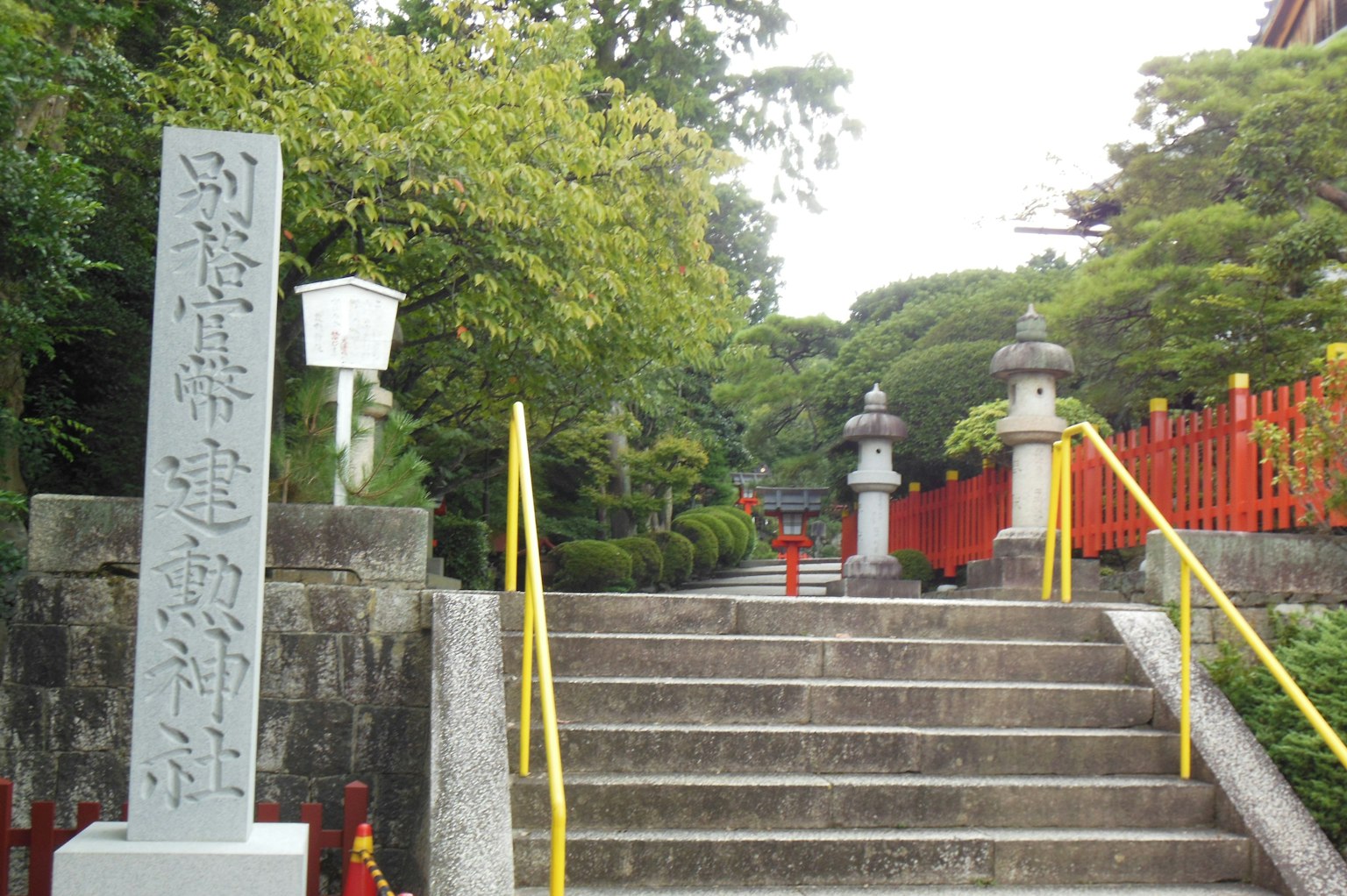神社的风景有石碑和台阶，周围环绕着绿色树木和红色栏杆