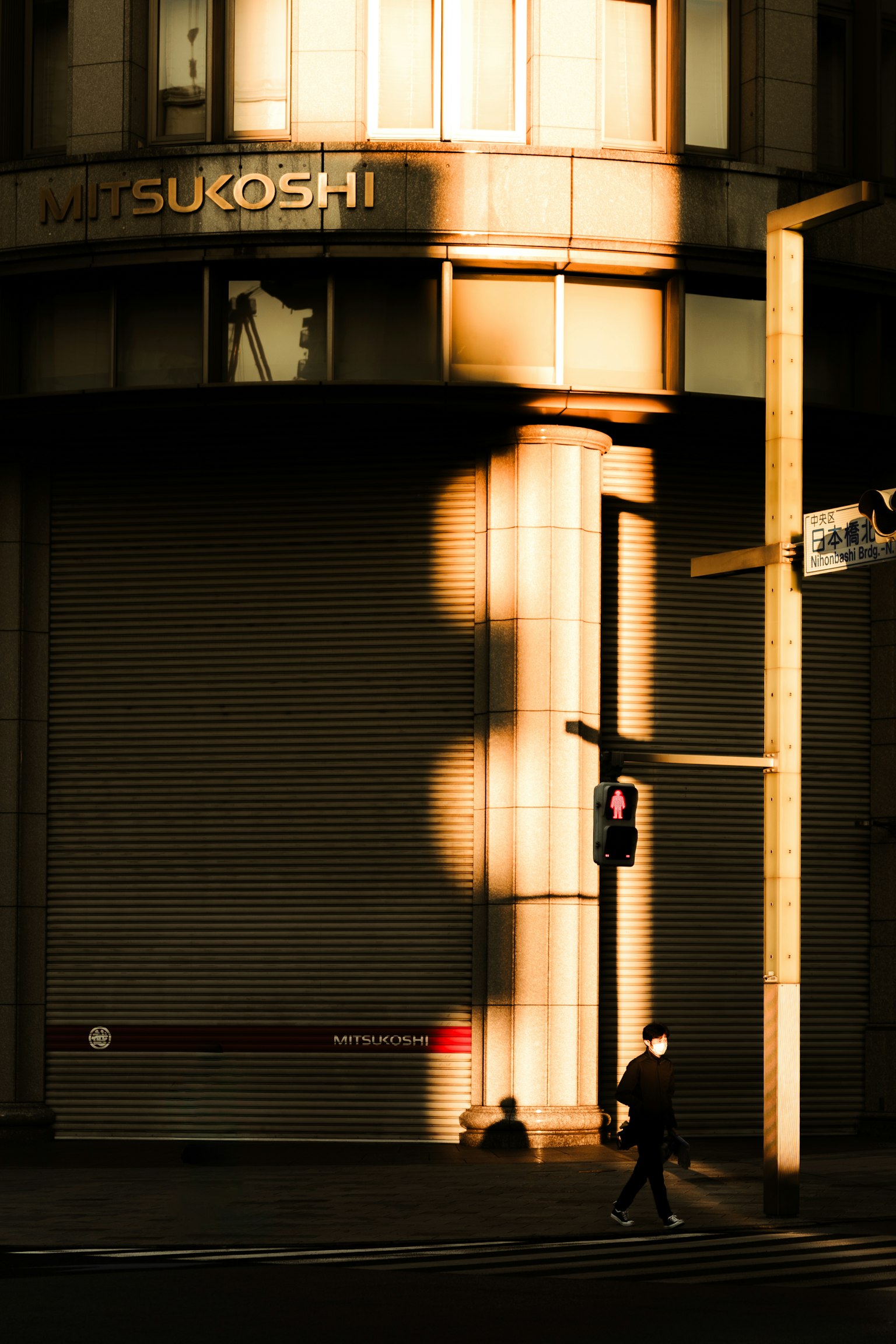Silueta de una persona caminando frente a un semáforo con sombras proyectadas sobre un edificio