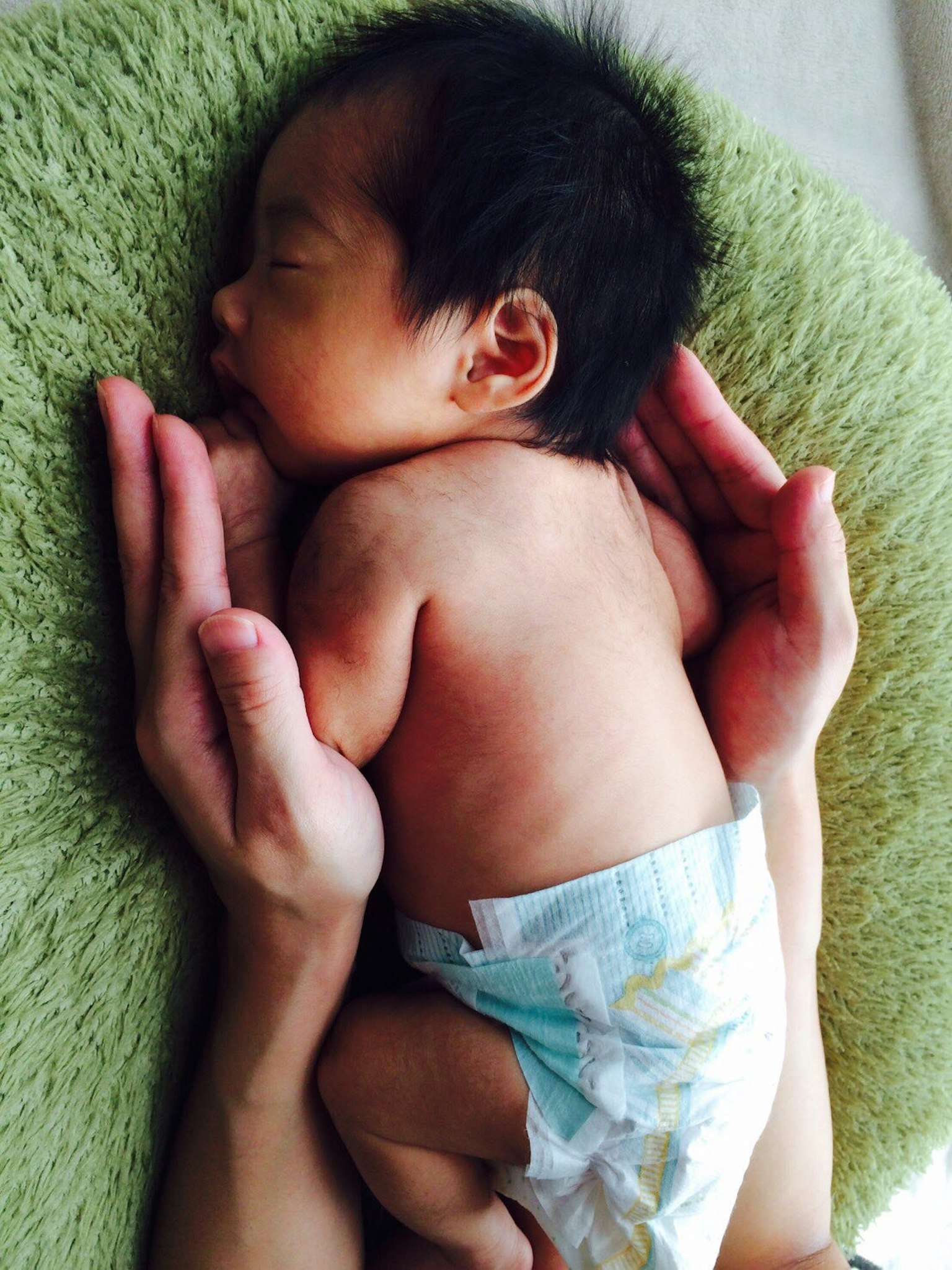Un bambino che dorme su mani con la schiena visibile che indossa un pannolino