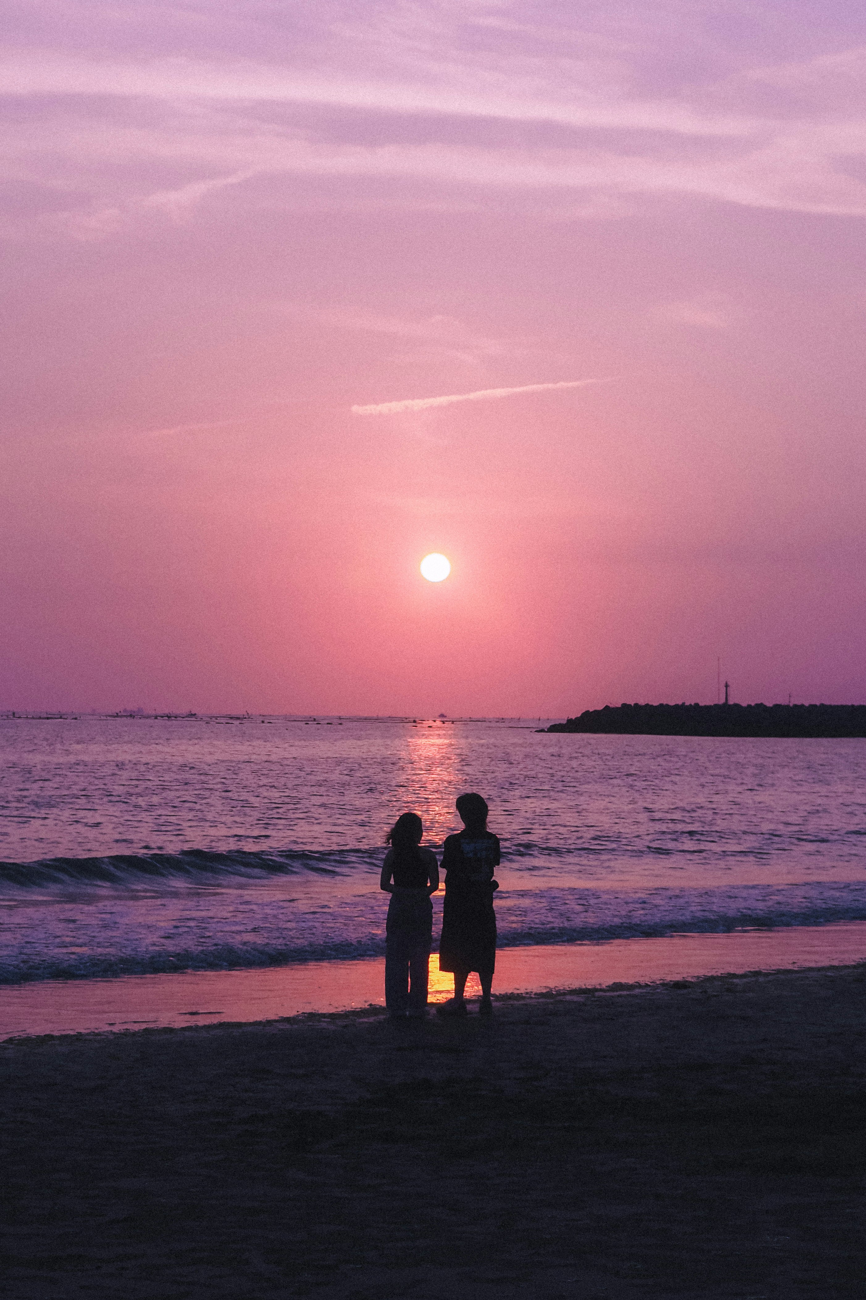 夕暮れの海辺で寄り添う人影