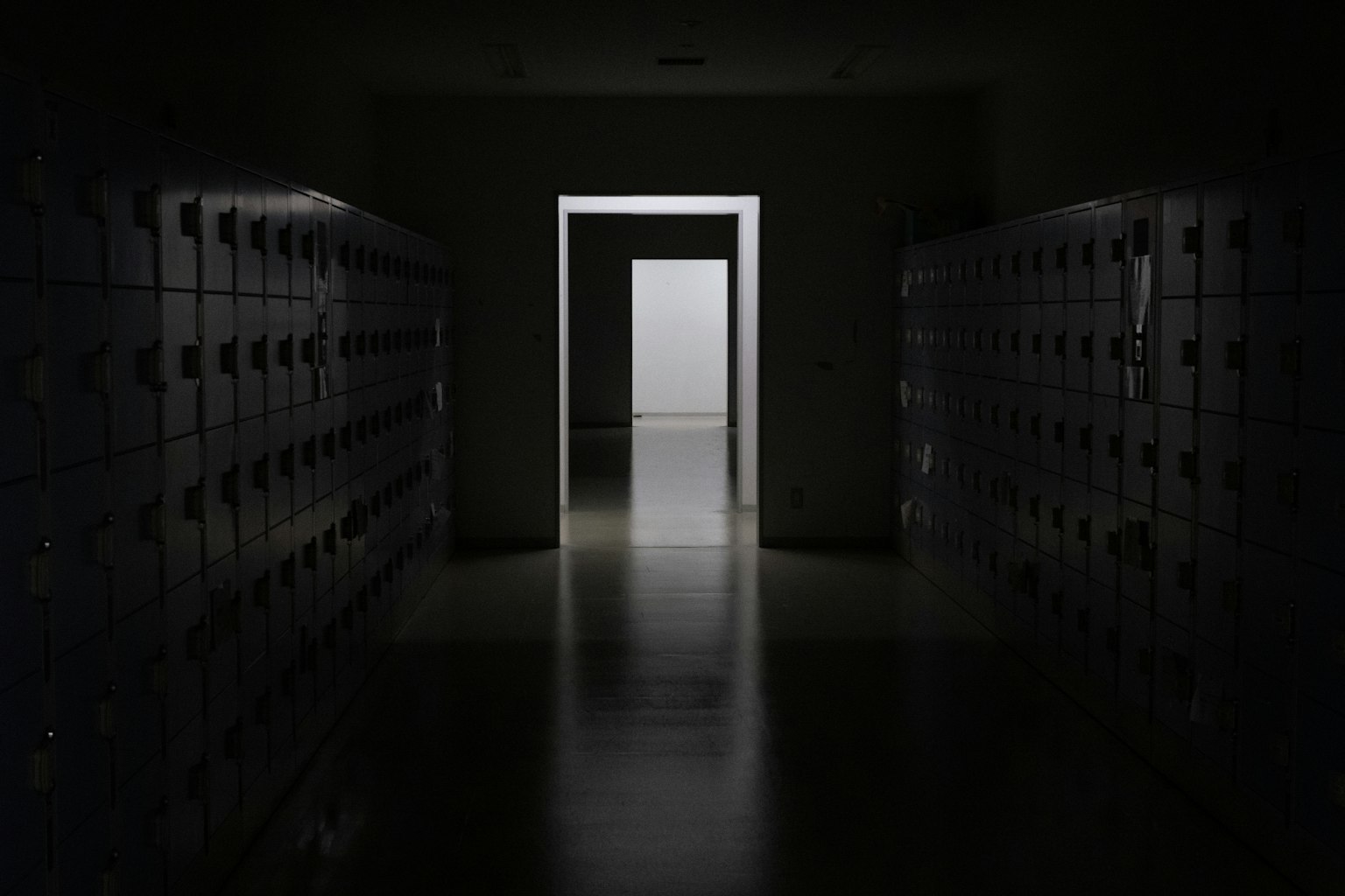 Corridoio buio fiancheggiato da armadietti e una porta luminosa