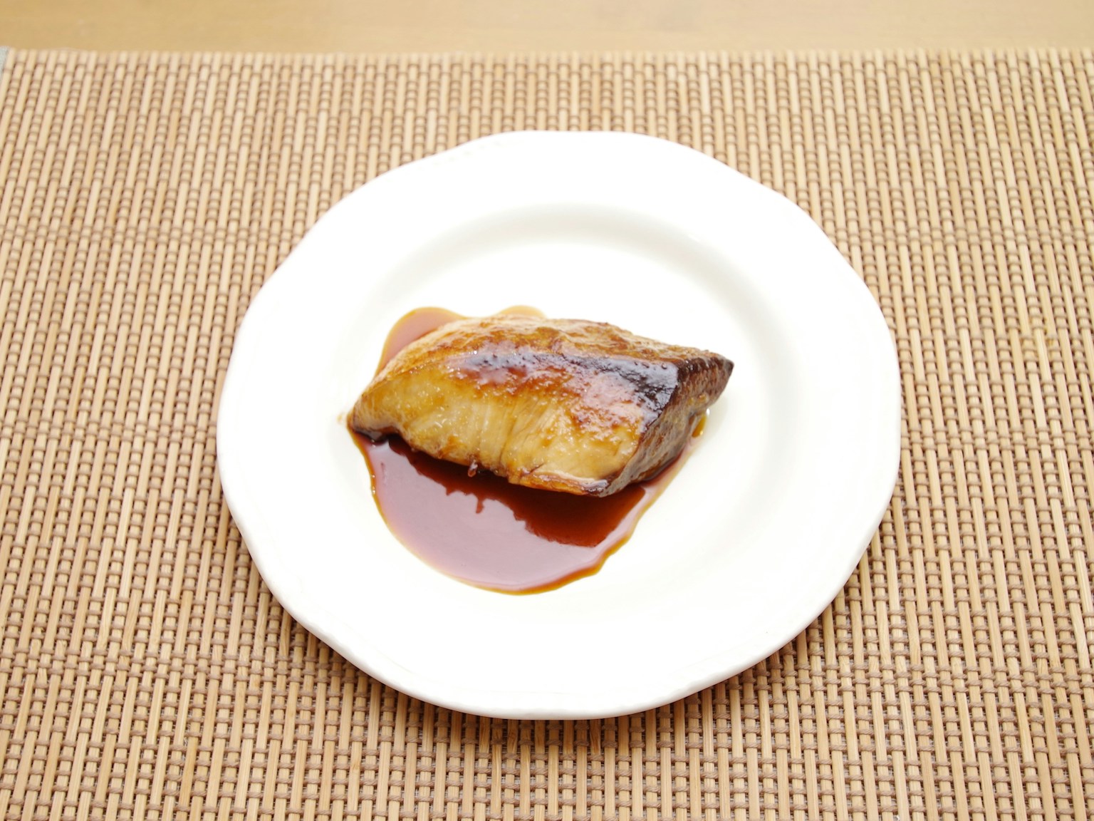 Filetto di pesce grigliato su un piatto bianco con una salsa dolce