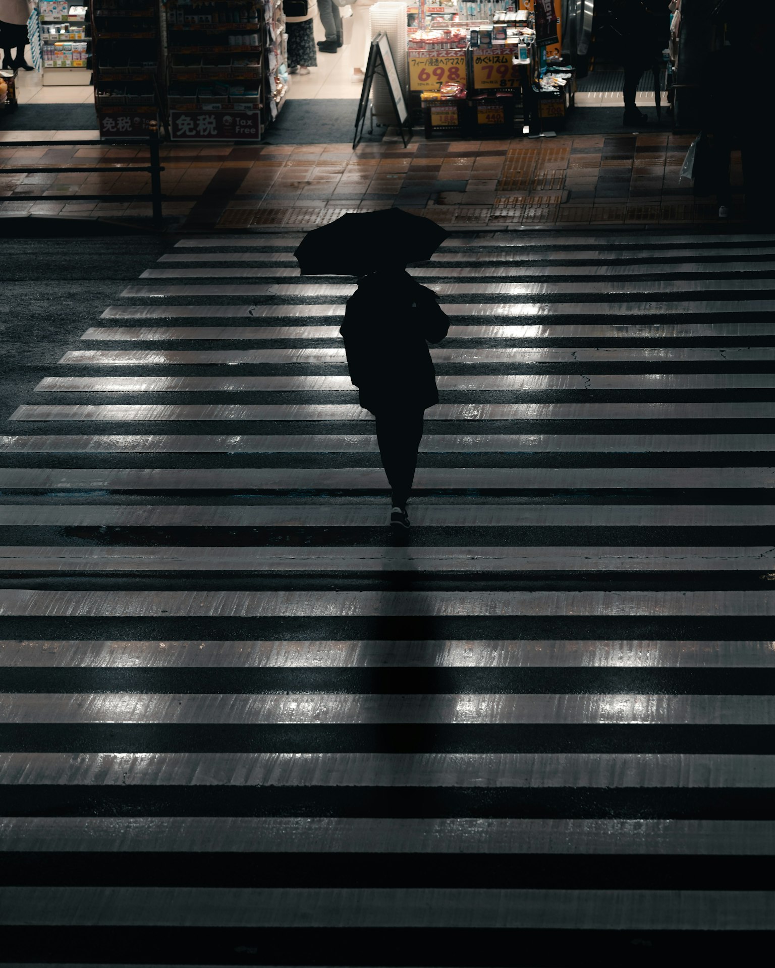 一个人拿着雨伞在夜晚的斑马线上走