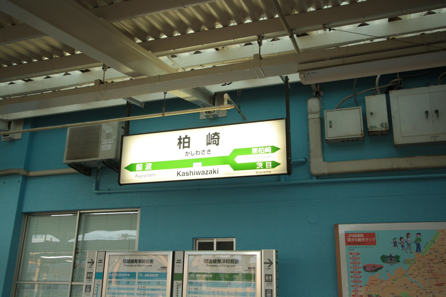 Image intérieure d'une gare avec un mur bleu et un panneau vert