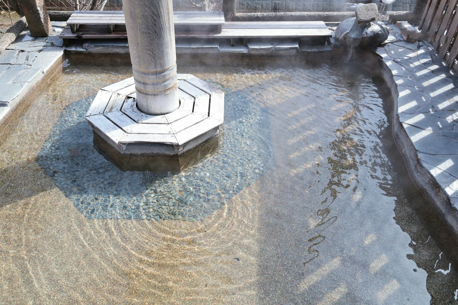Scena di un pilastro ottagonale in pietra vicino a una sorgente termale con superficie d'acqua chiara