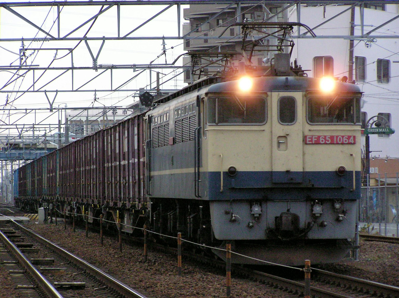 Blue freight train stopped at a station with overhead wires