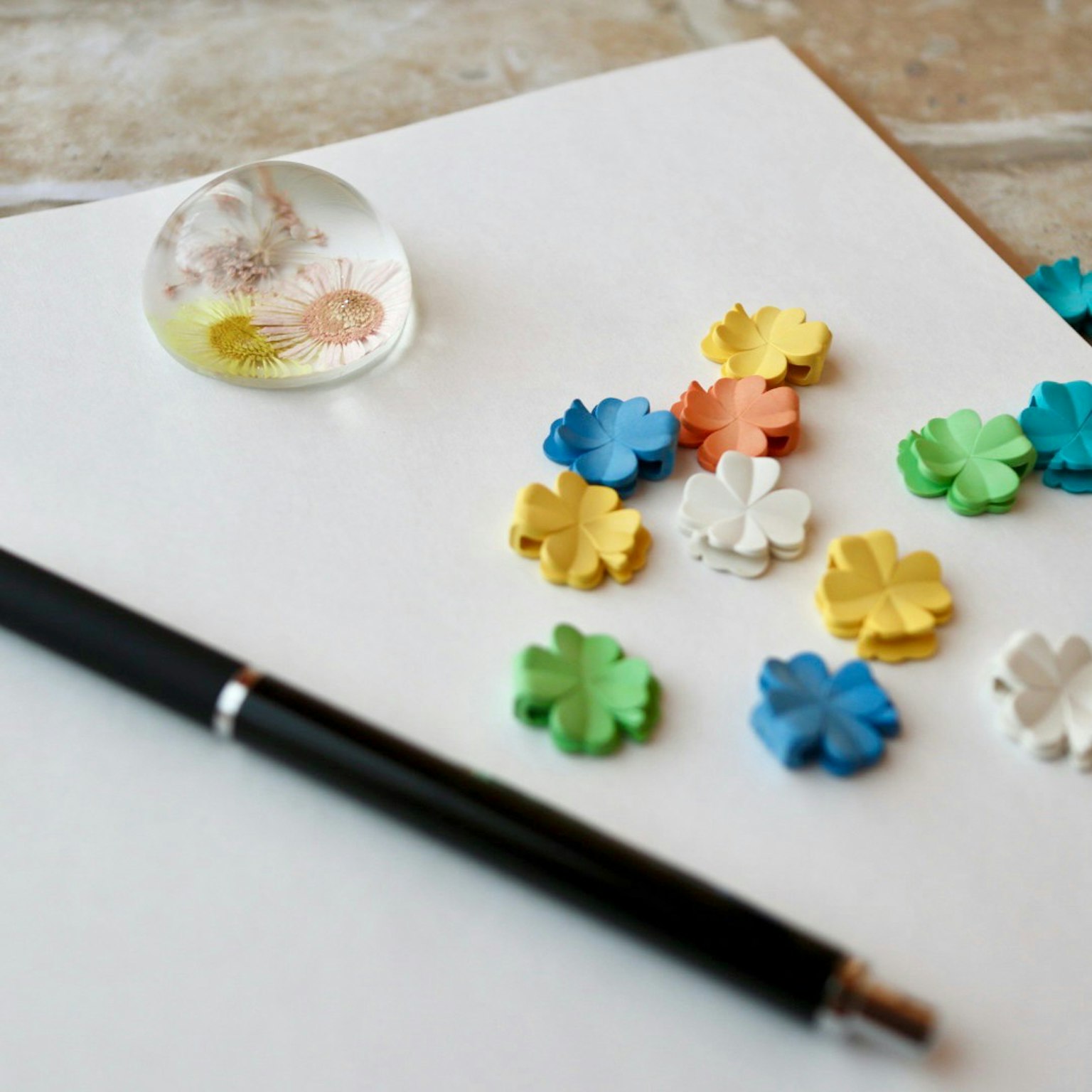 Decorazioni a forma di fiore colorate e una penna su carta bianca