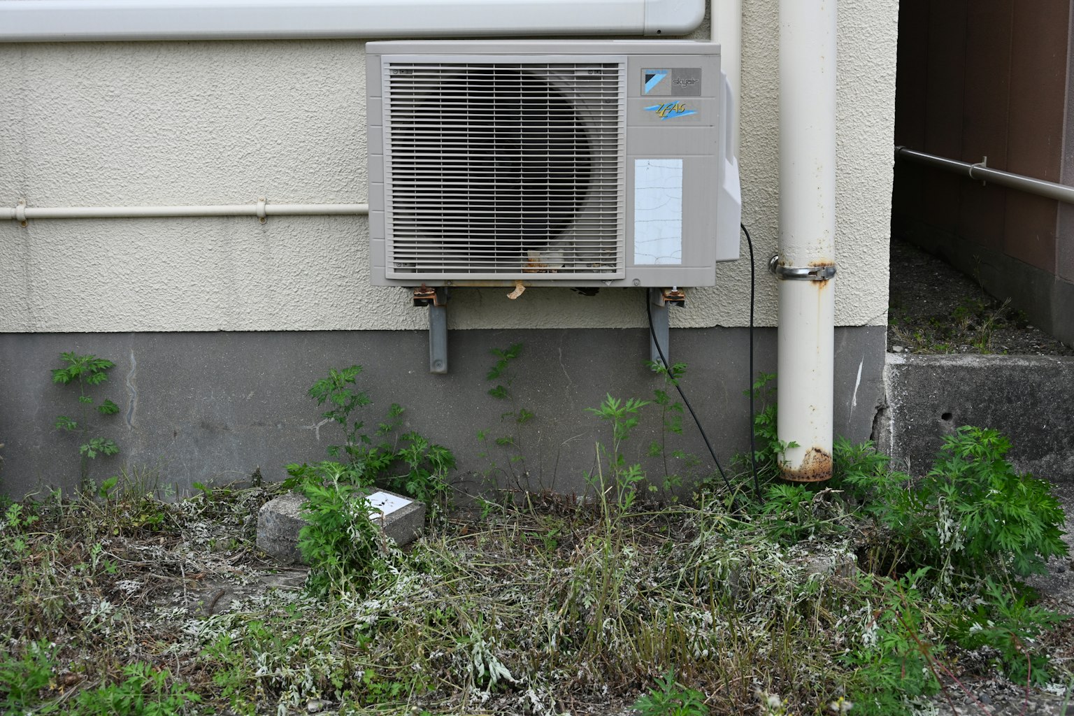 Unité de climatisation montée sur un mur avec de l'herbe envahie autour