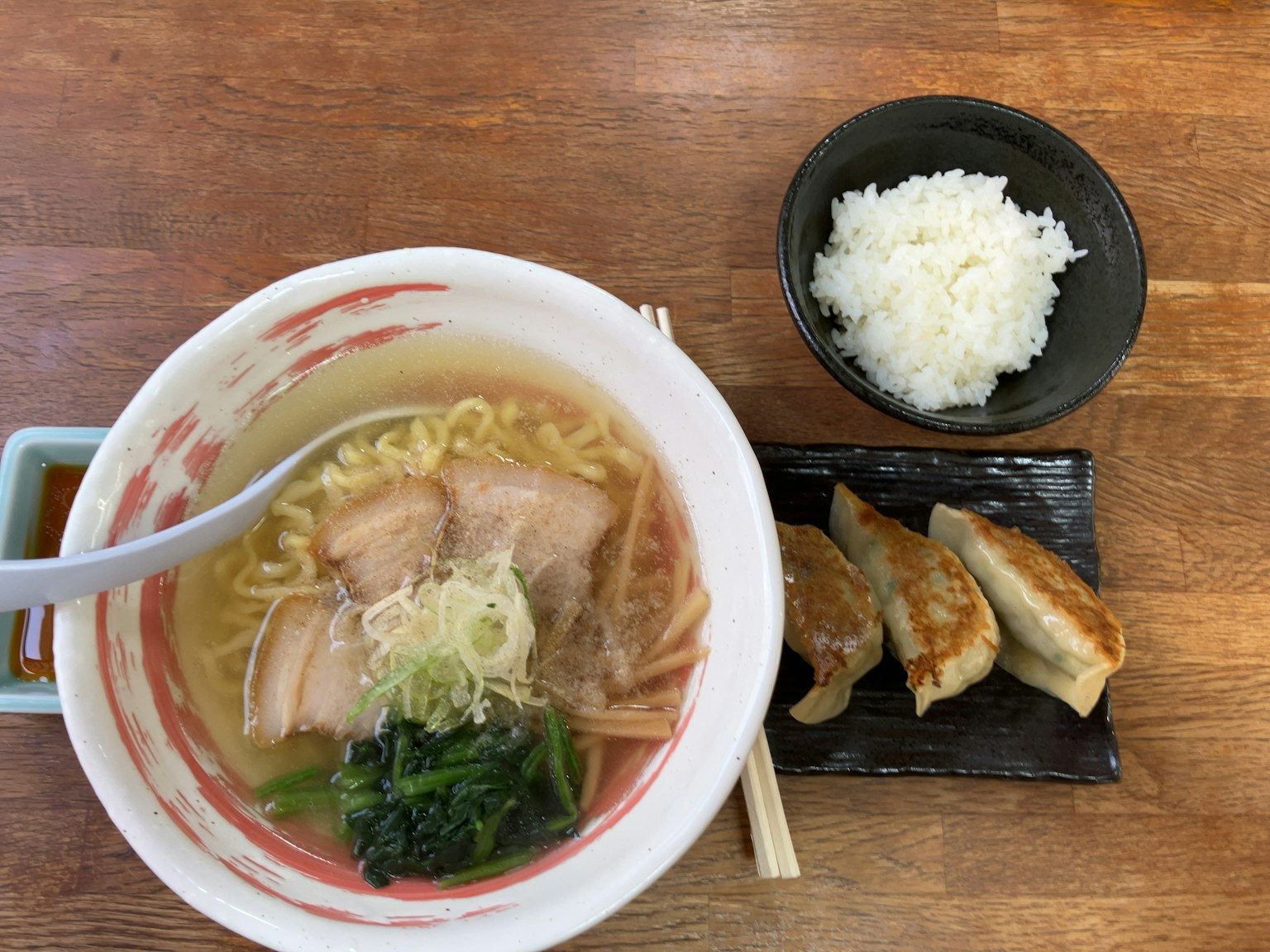 一碗拉面，配有切片猪肉、葱、菠菜，旁边有饺子和米饭