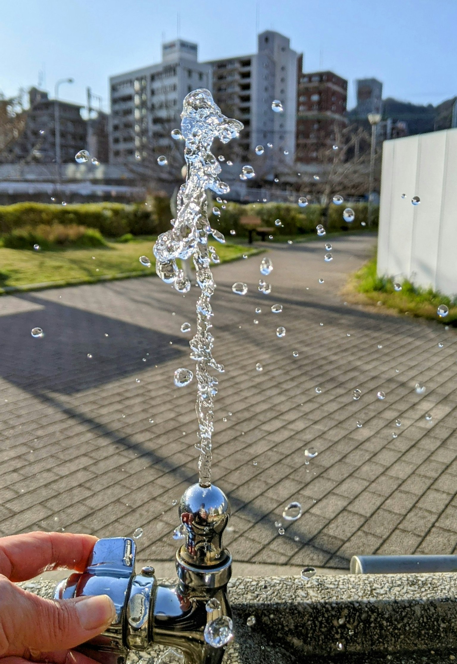 Eau jaillissant d'un robinet avec un ciel bleu clair et des bâtiments en arrière-plan