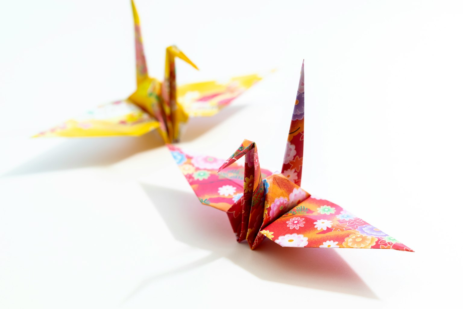 Zwei bunte Origami-Kraniche aus gemustertem Papier
