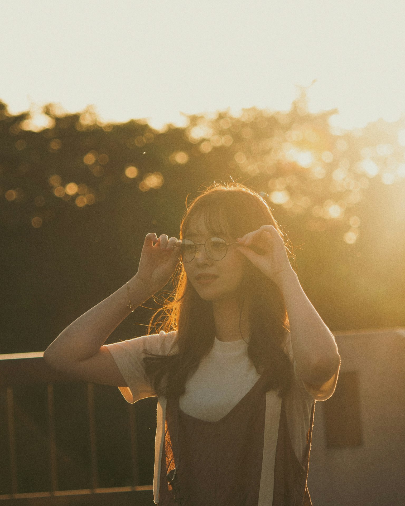Une femme souriante tenant ses lunettes avec le coucher de soleil en arrière-plan