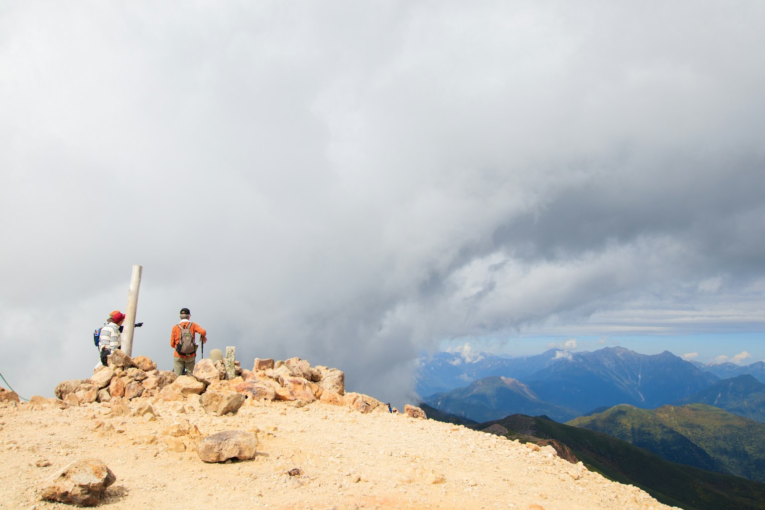 Zwei Wanderer stehen auf einem Berggipfel bei bewölktem Himmel