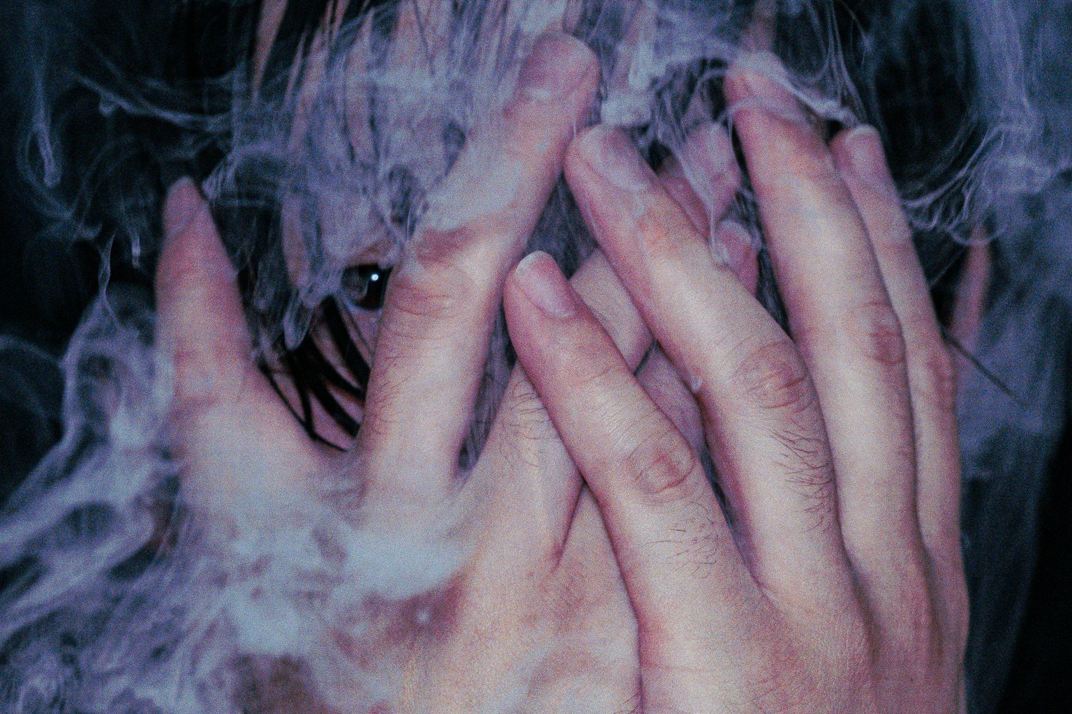 手で顔を隠す人物のクローズアップ写真 背景に煙のような効果