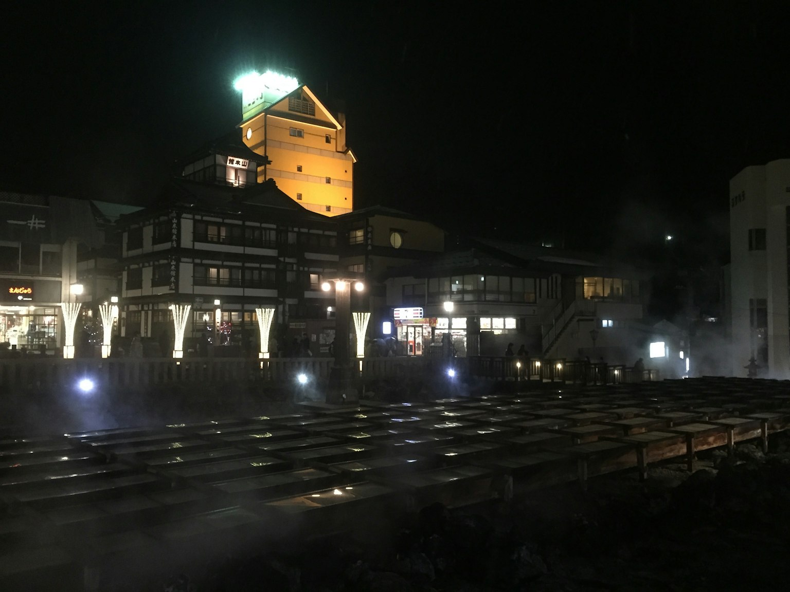 Night view of a hot spring town featuring illuminated buildings and steam rising from the hot springs