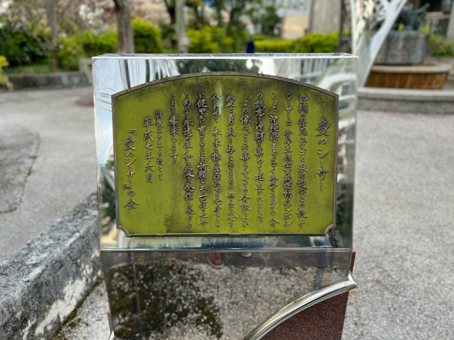 A polished metal plaque with engraved text in a park setting