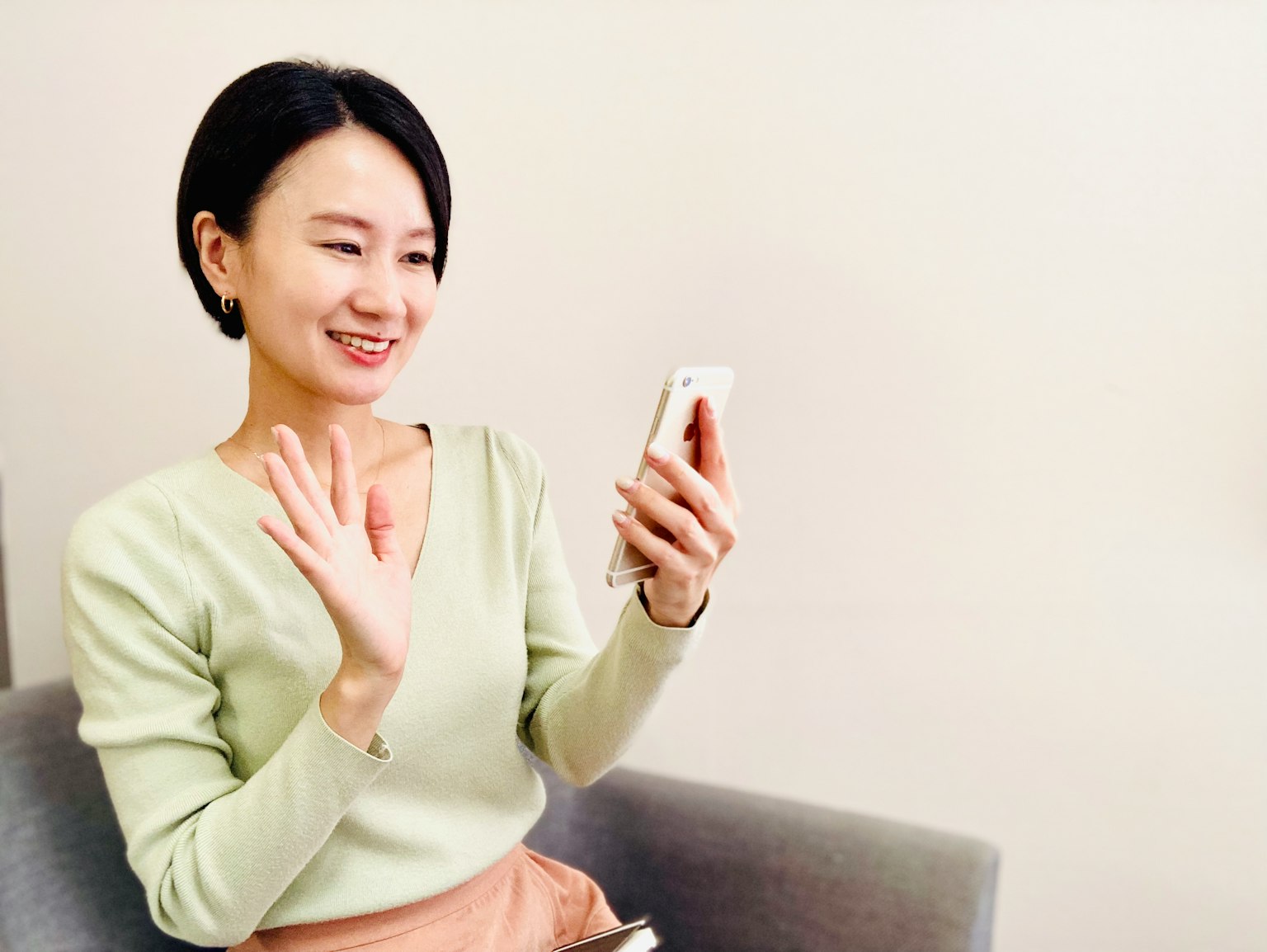 Una donna in maglione verde che sorride e saluta il suo smartphone