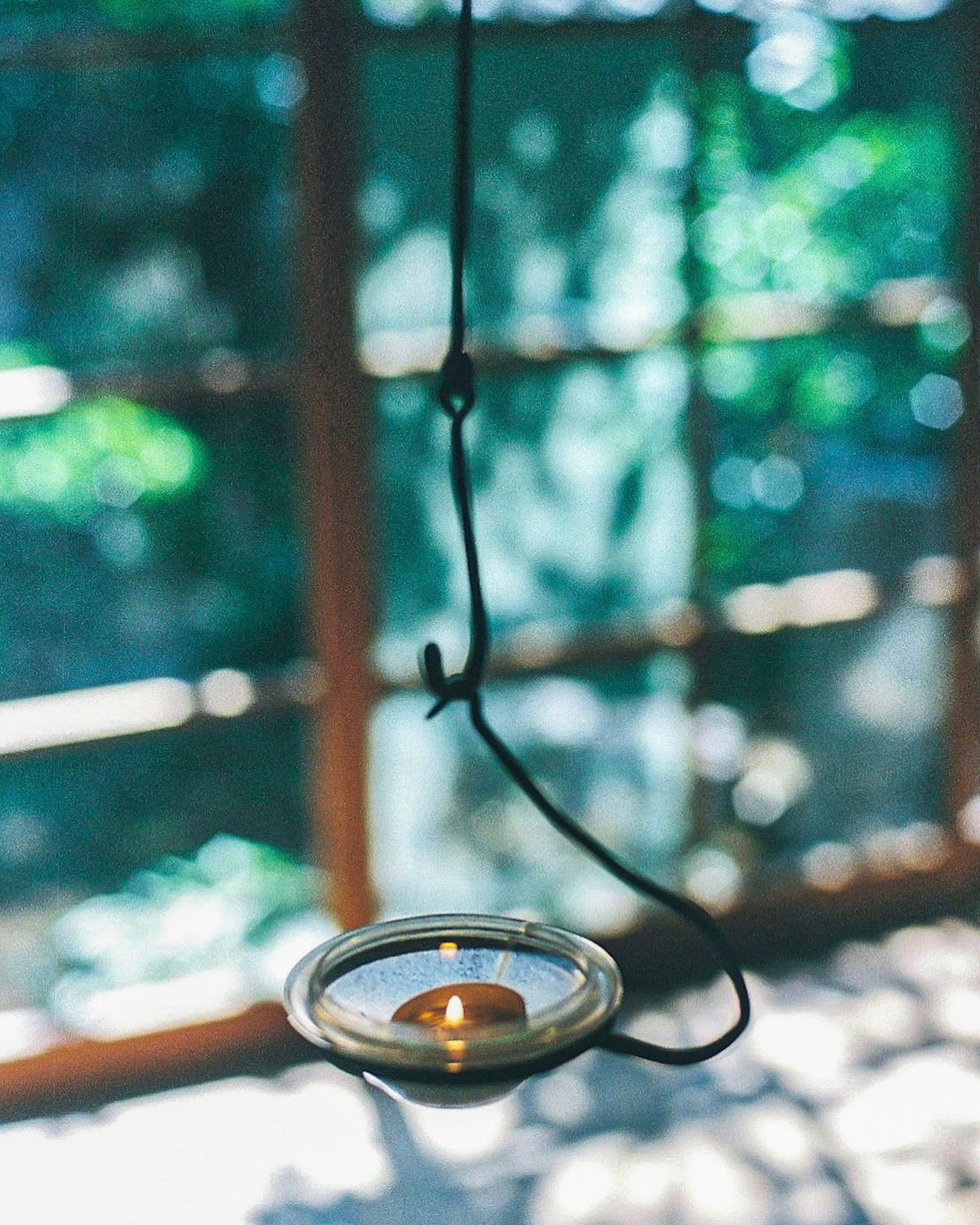 Portavelas colgante con vela encendida y fondo verde borroso