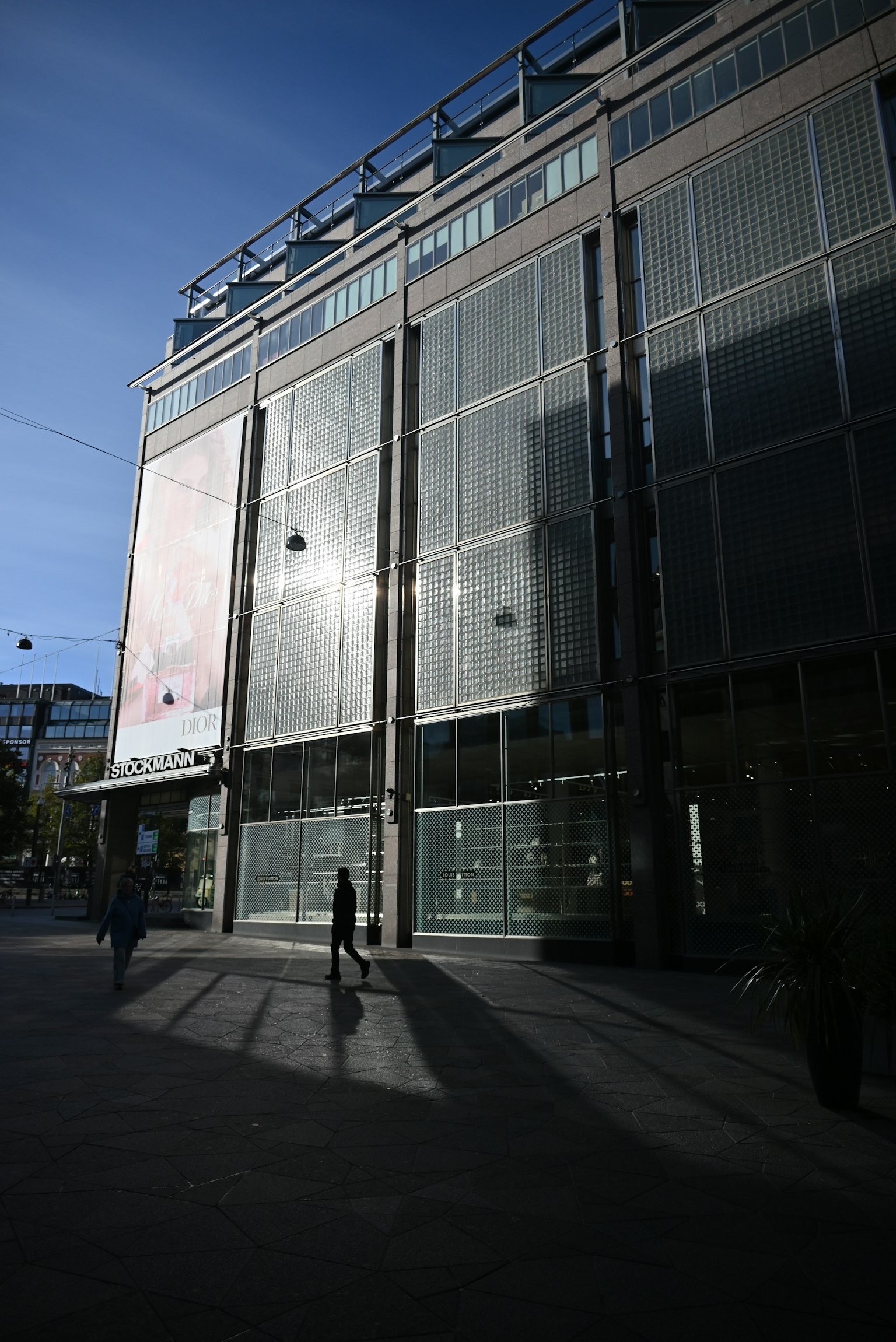 Fachada de un edificio moderno con reflejos en un paisaje urbano Una persona caminando con sombras en el suelo
