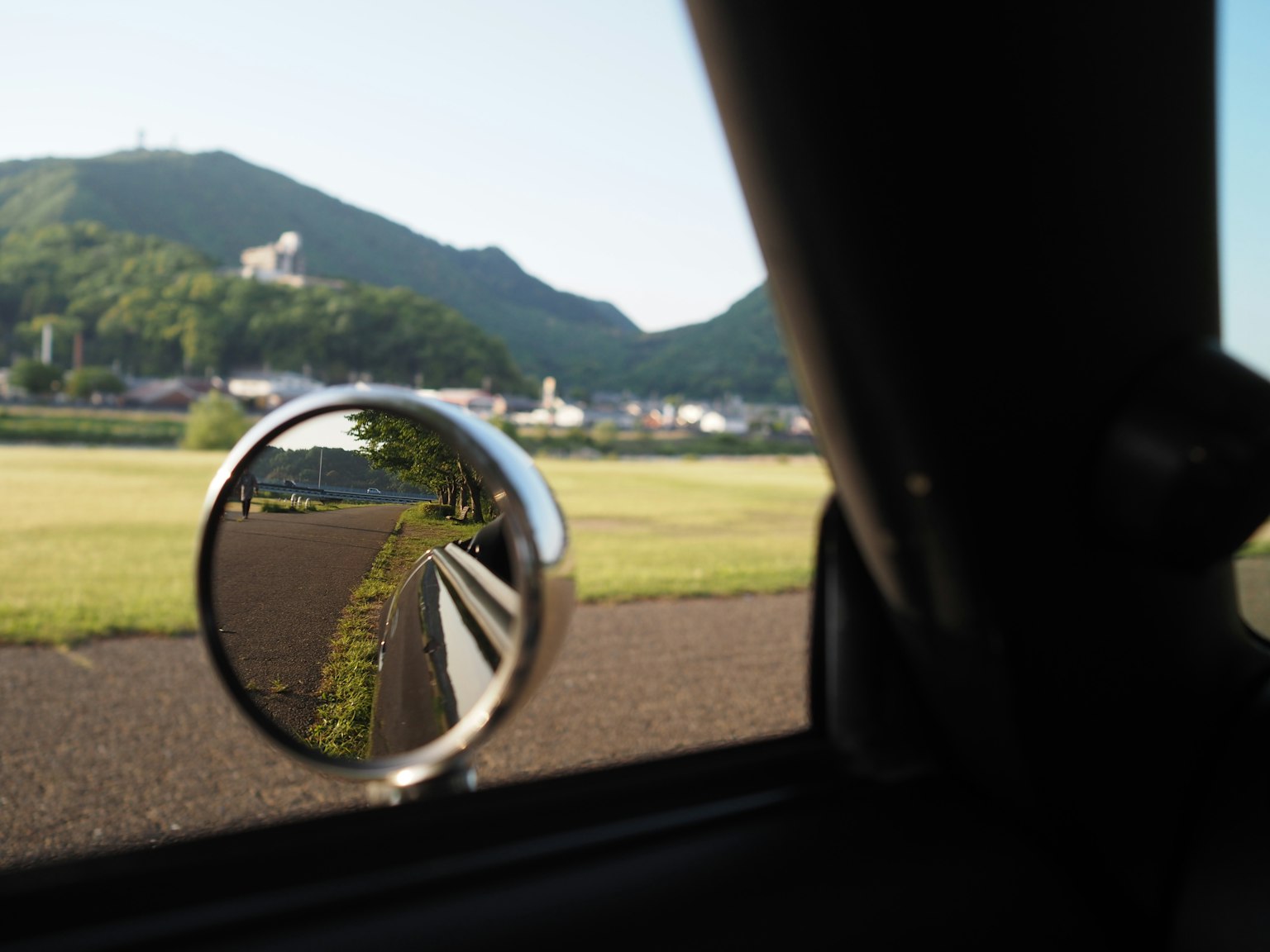 Vista panoramica riflessa in uno specchietto laterale di un'auto con montagne sullo sfondo