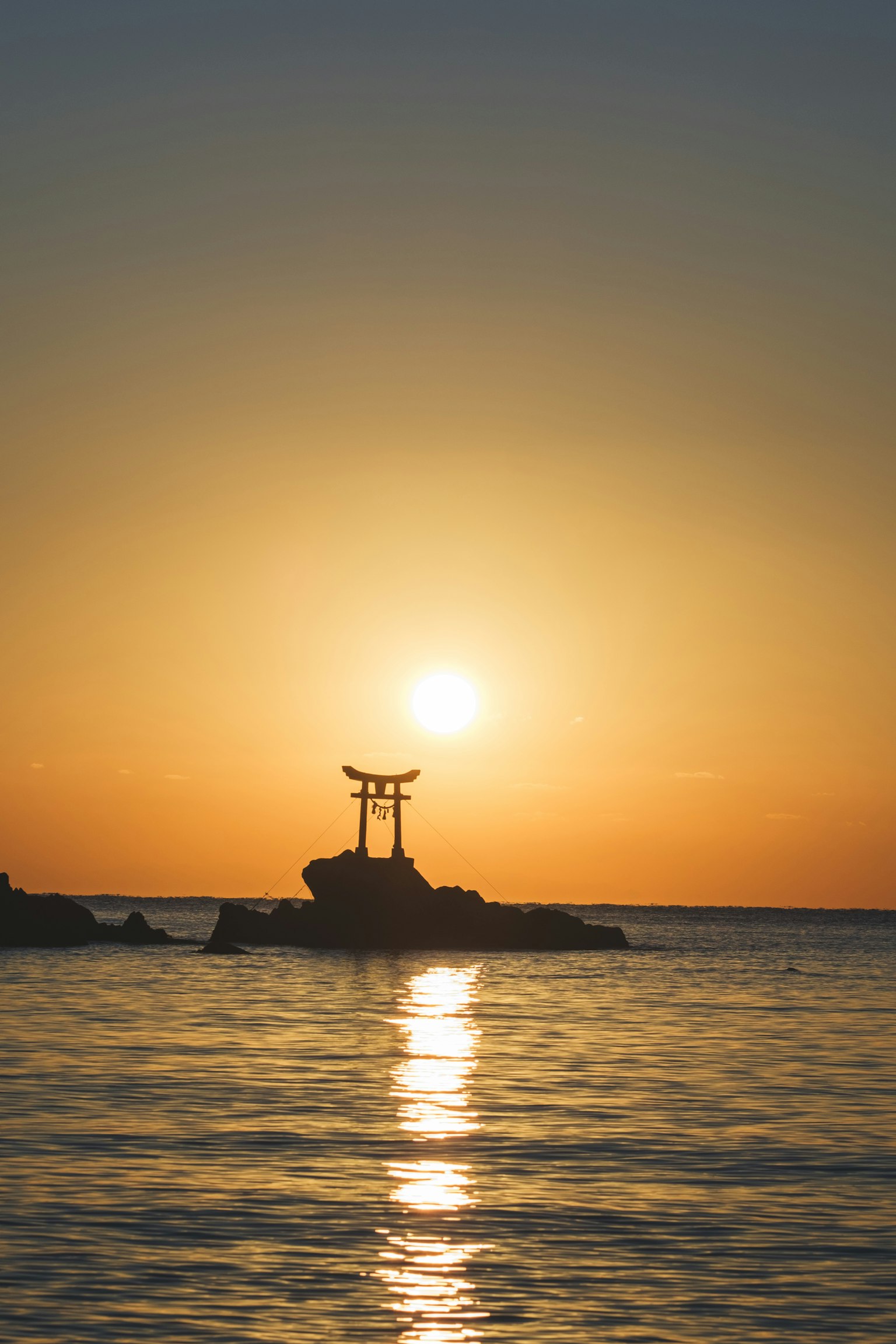 A serene sunset view with a torii gate silhouetted against the sea