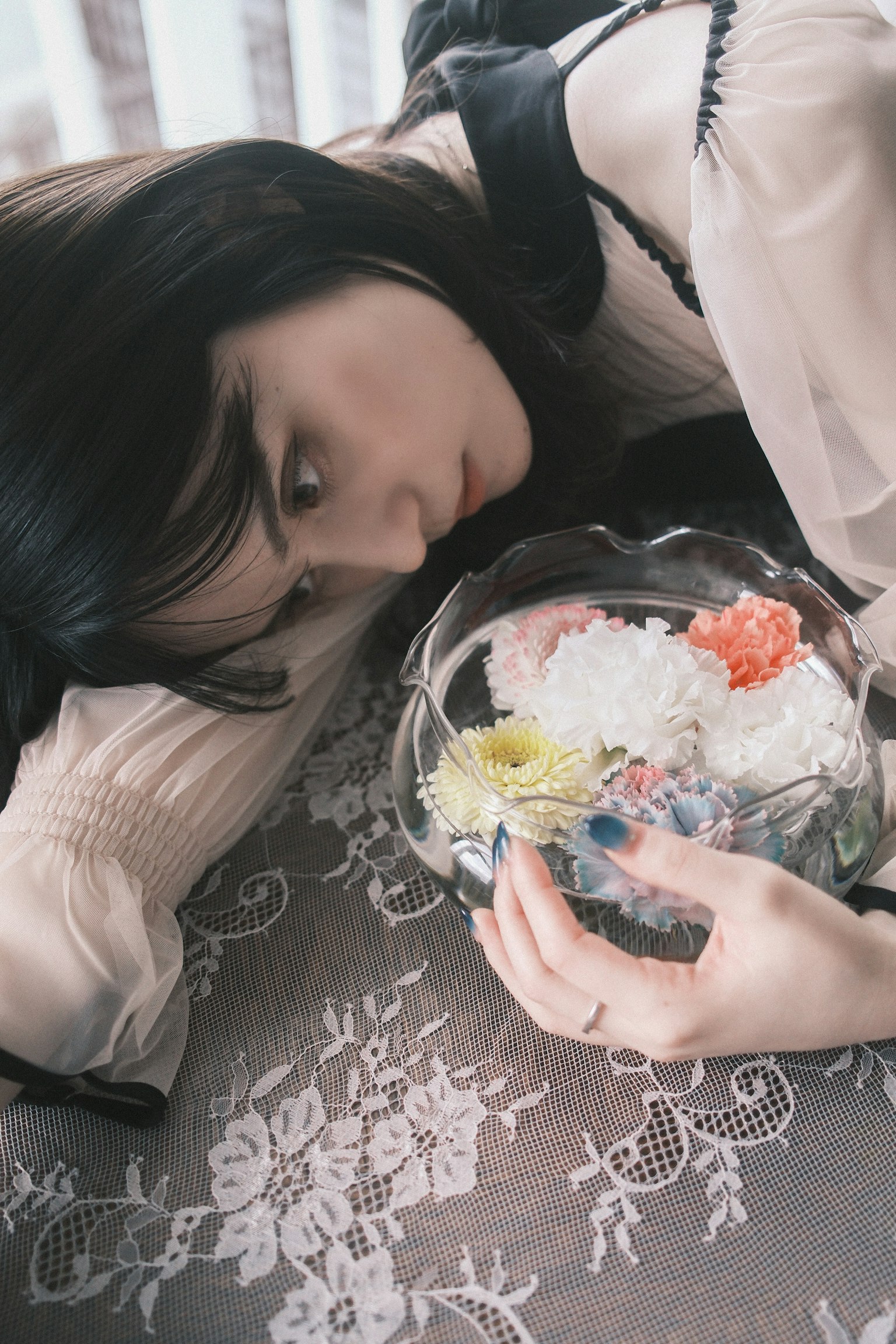 女性が花の入ったガラスのボウルを持ちながら横たわっているシーン