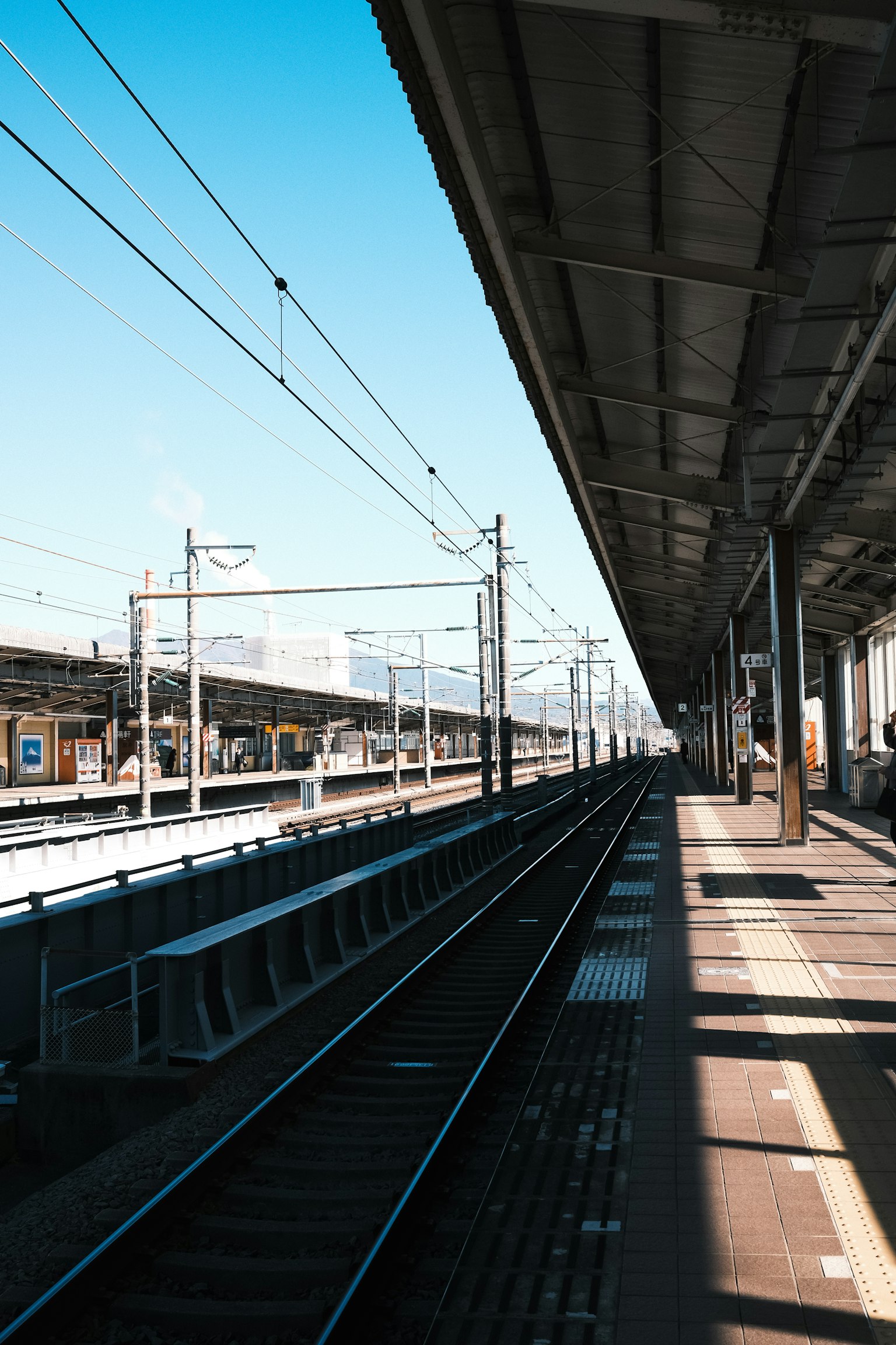 Plateforme de gare sous un ciel bleu clair avec des voies ferrées et des ombres