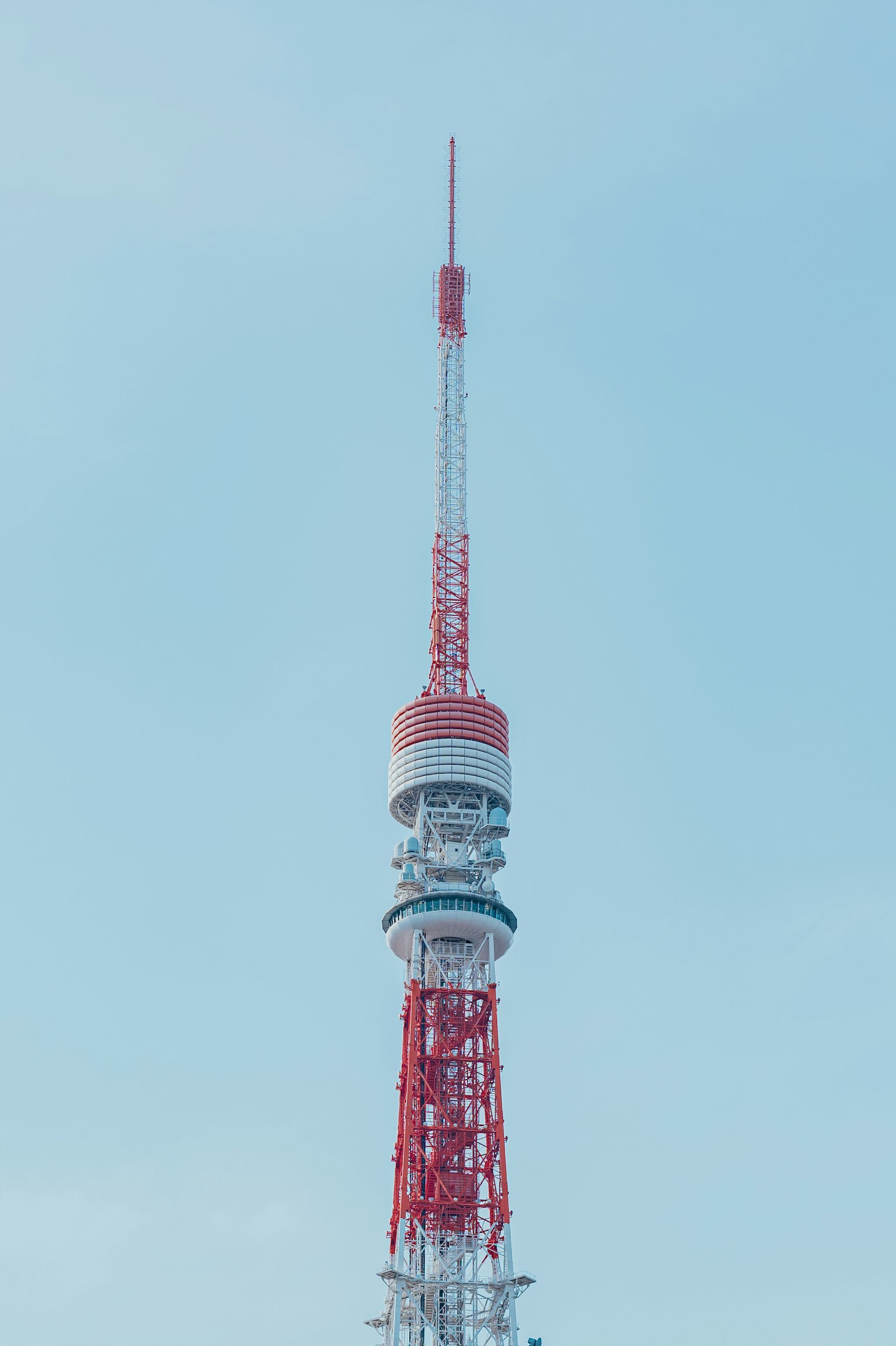 Top of a red and white communication tower against a blue sky