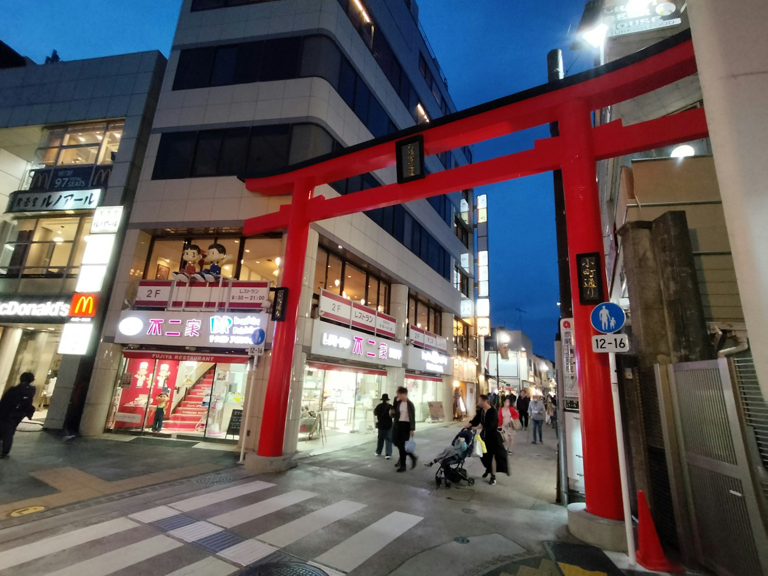 Vista nocturna de una calle animada con una puerta torii roja