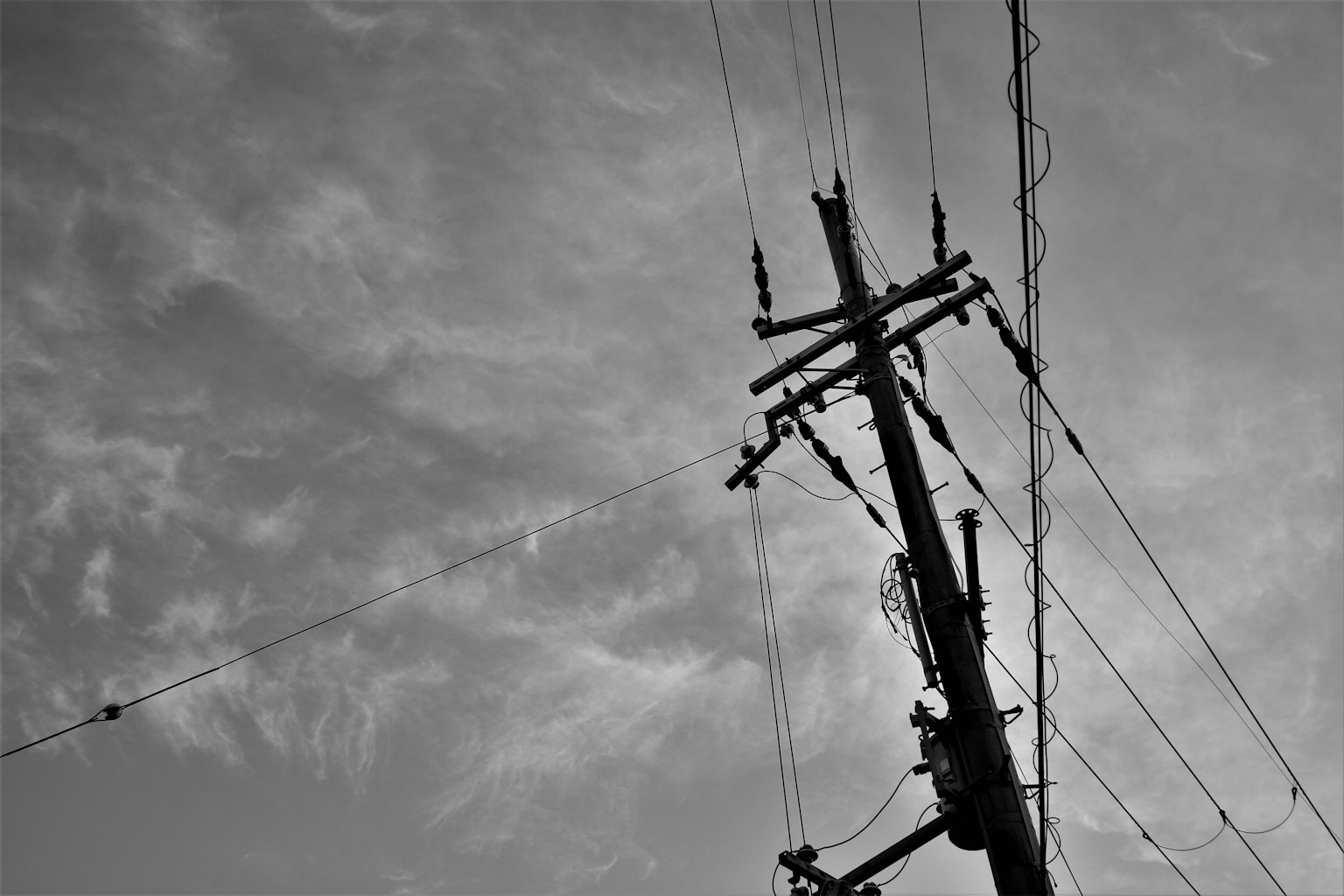 Siluet tiang listrik dengan kabel di latar belakang langit berawan