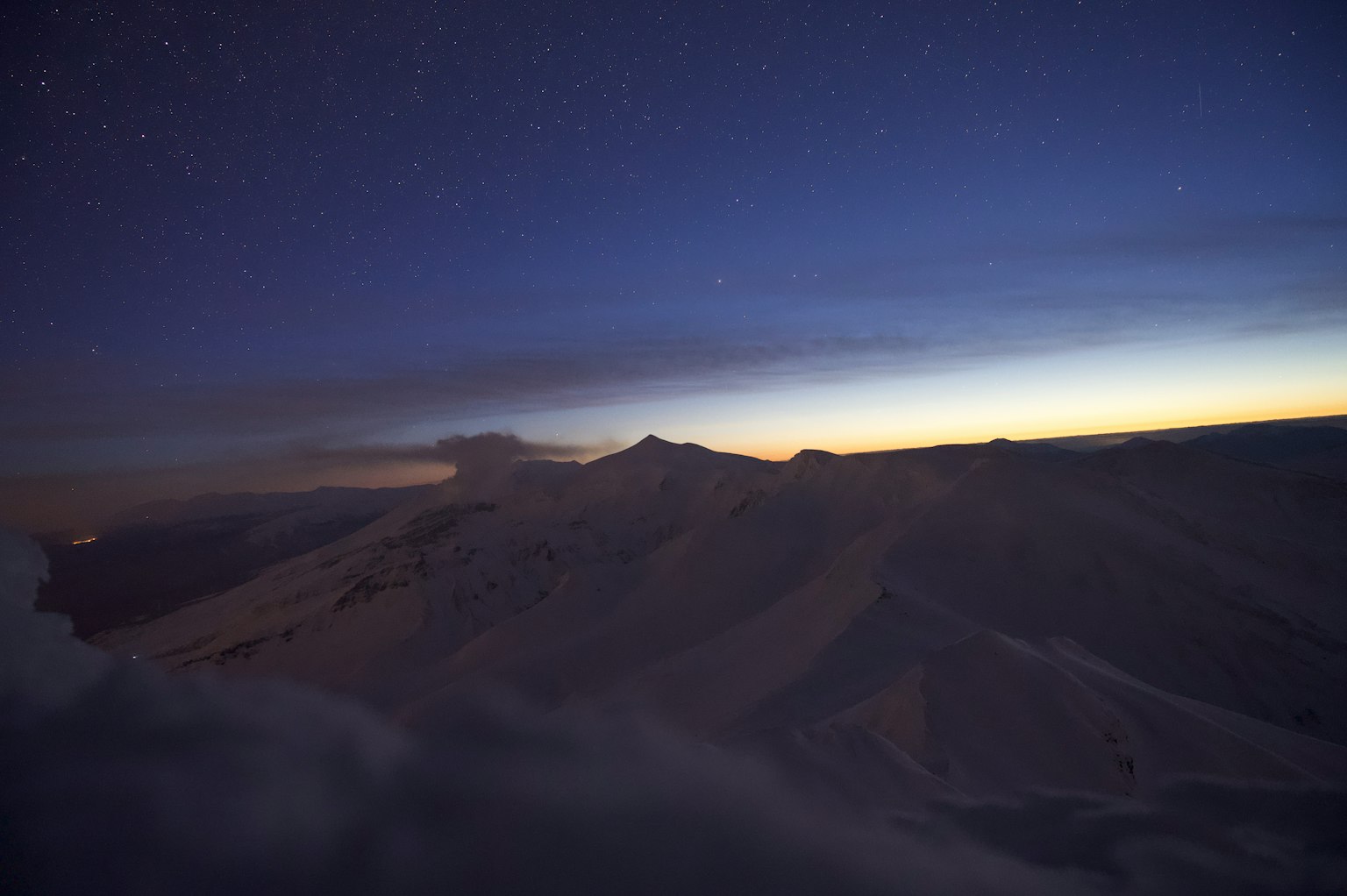 Silueta de montañas bajo un cielo estrellado con luz del amanecer
