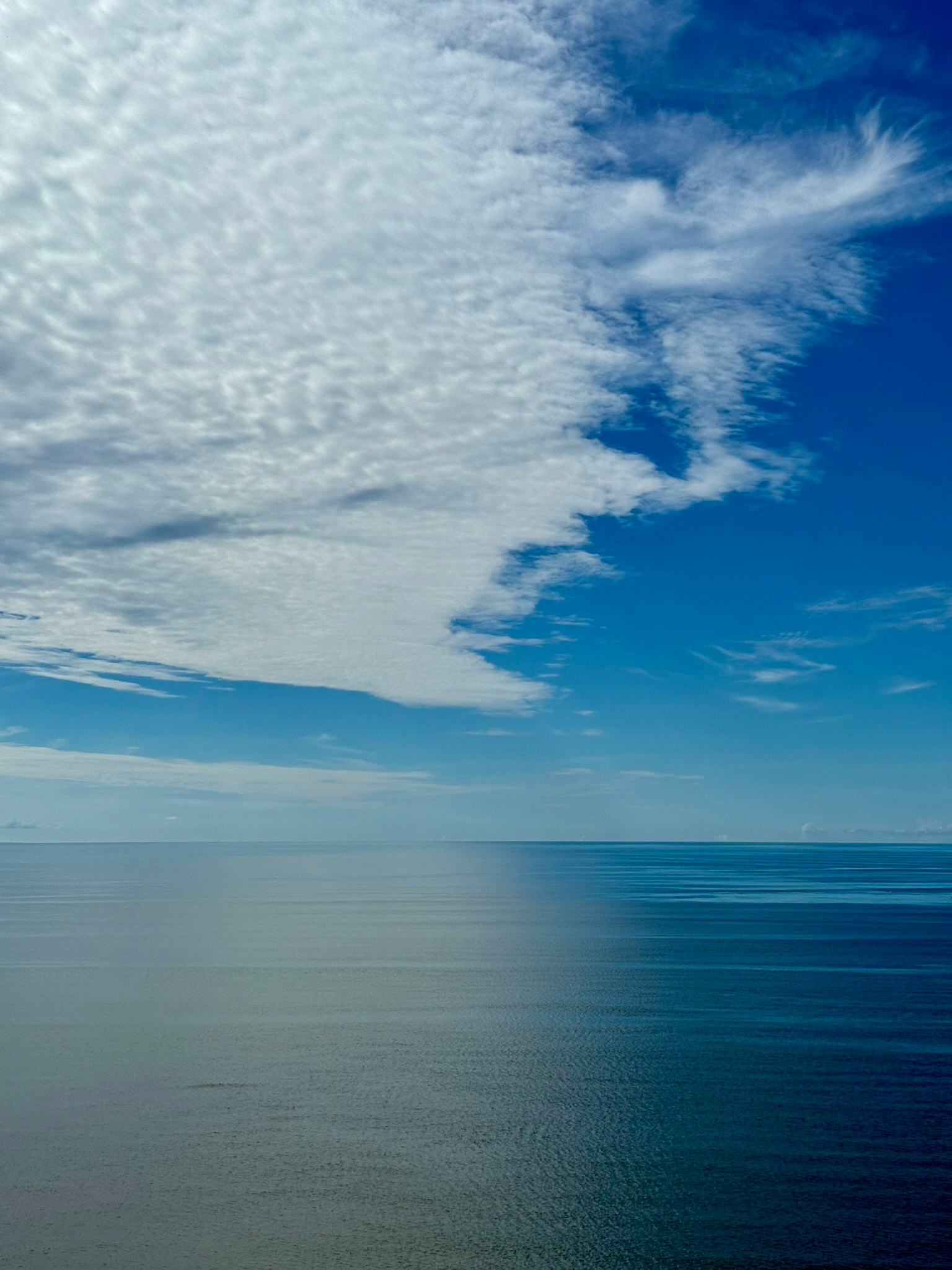 A serene view of the ocean meeting the sky with distinct cloud patterns