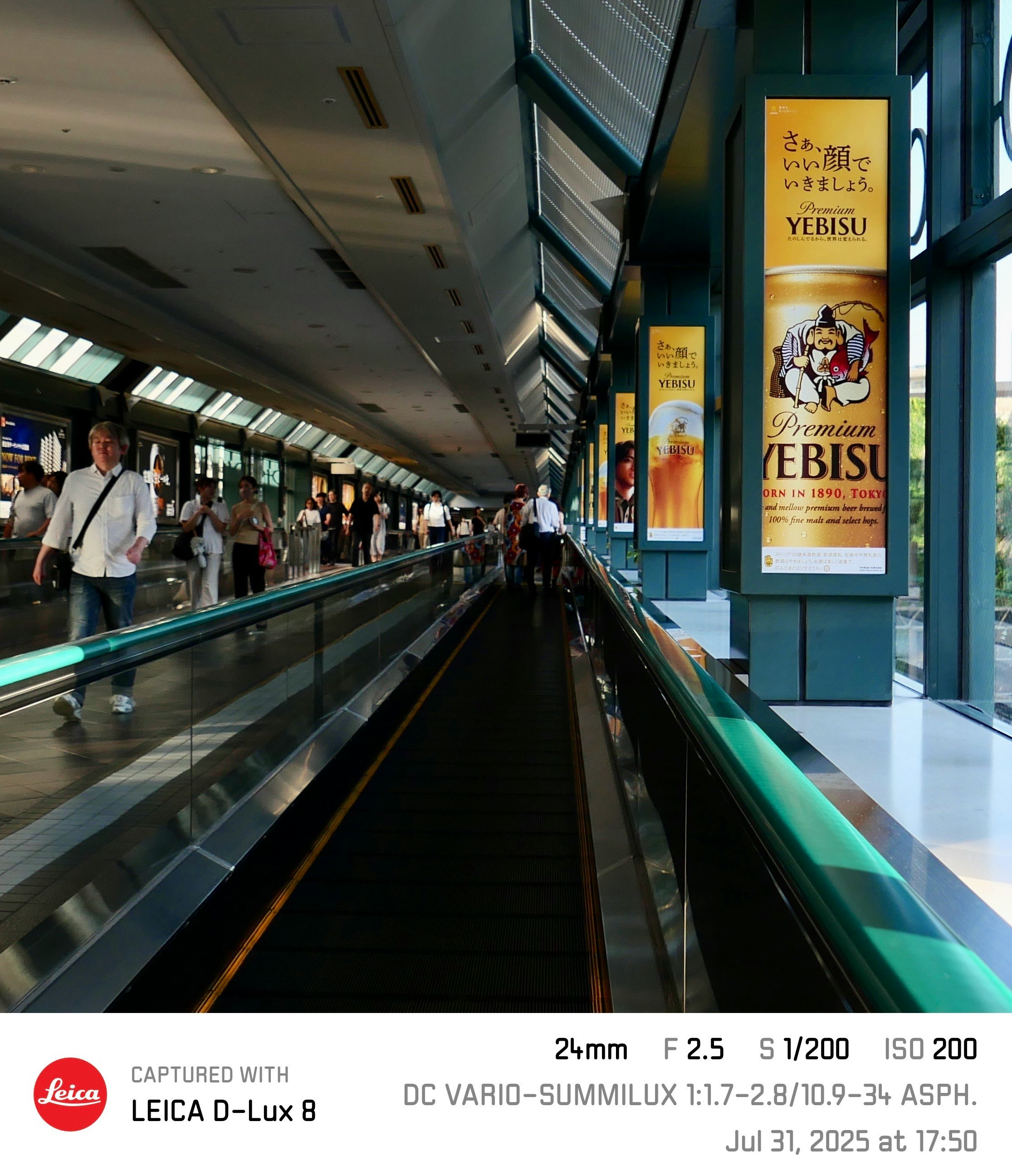 駅構内の壁に掲げられたビール広告ポスターと人々の行き交う通路