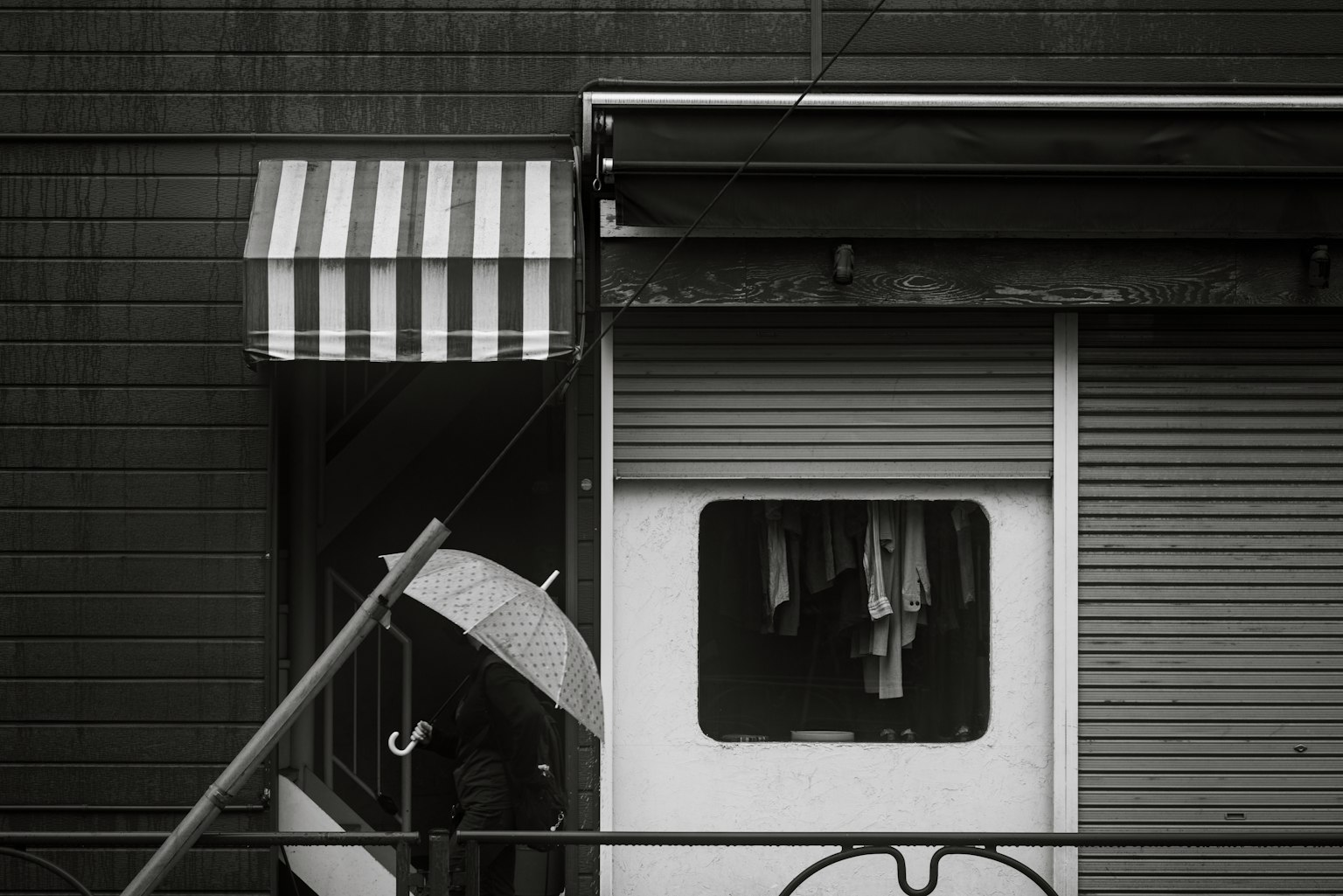 Section of a building featuring a striped awning and a shuttered window