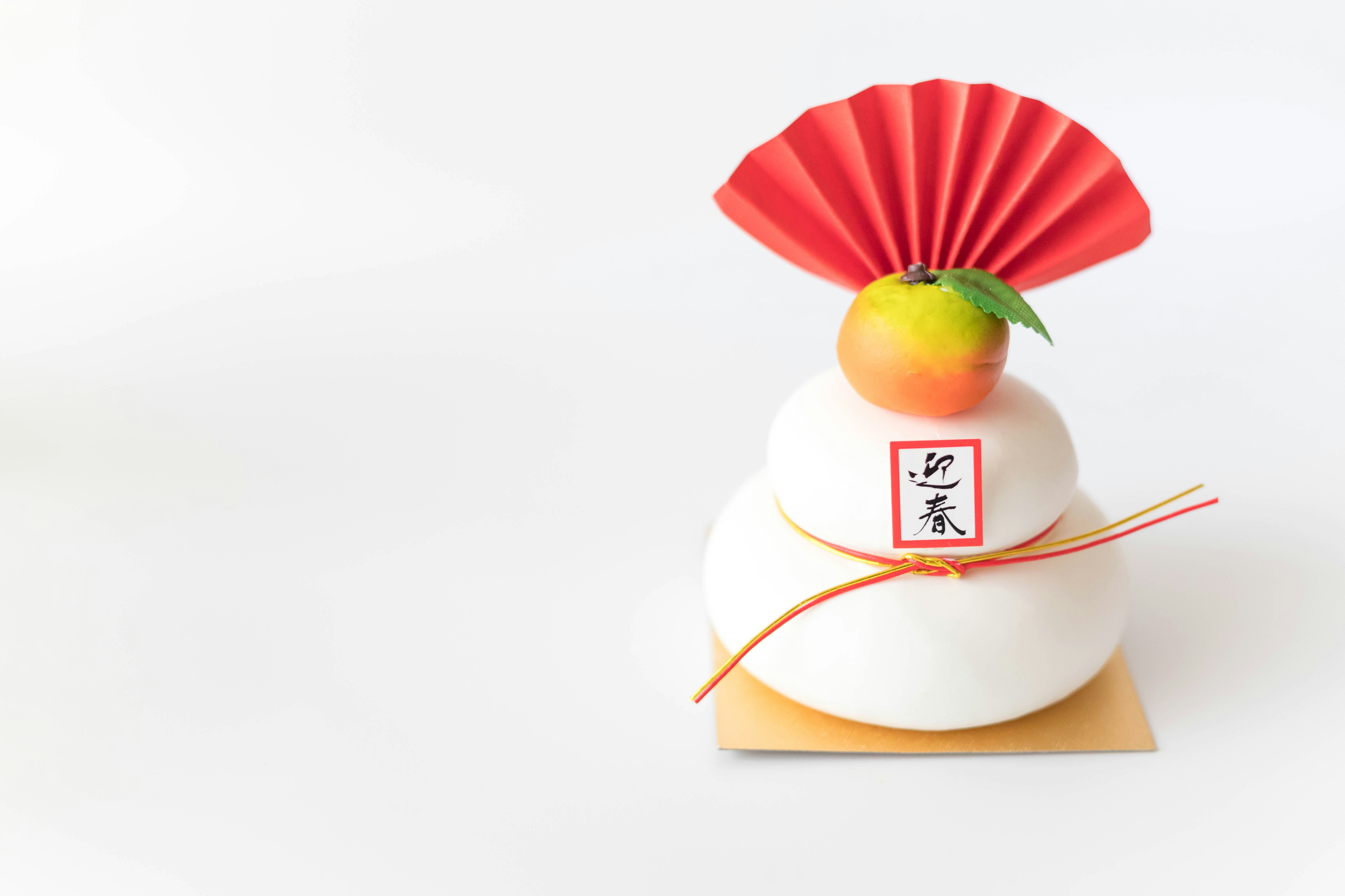 Kue gaya Tahun Baru Jepang dengan kipas lipat merah dan dekorasi plum di latar putih