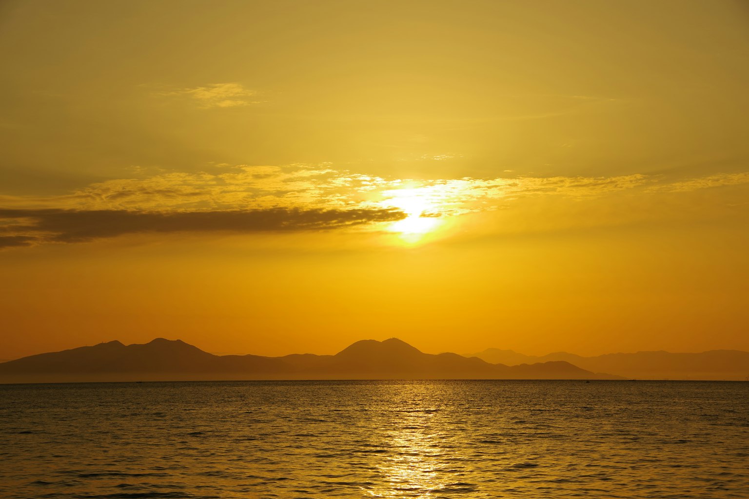 Pemandangan matahari terbenam yang indah di atas lautan dengan langit oranye dan pegunungan