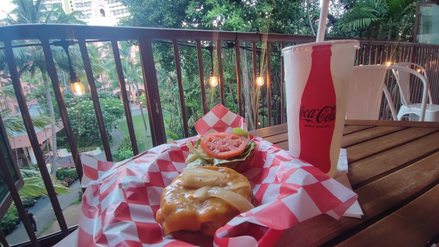Gros plan sur un hamburger et une boisson sur une table en bois avec des plantes en arrière-plan