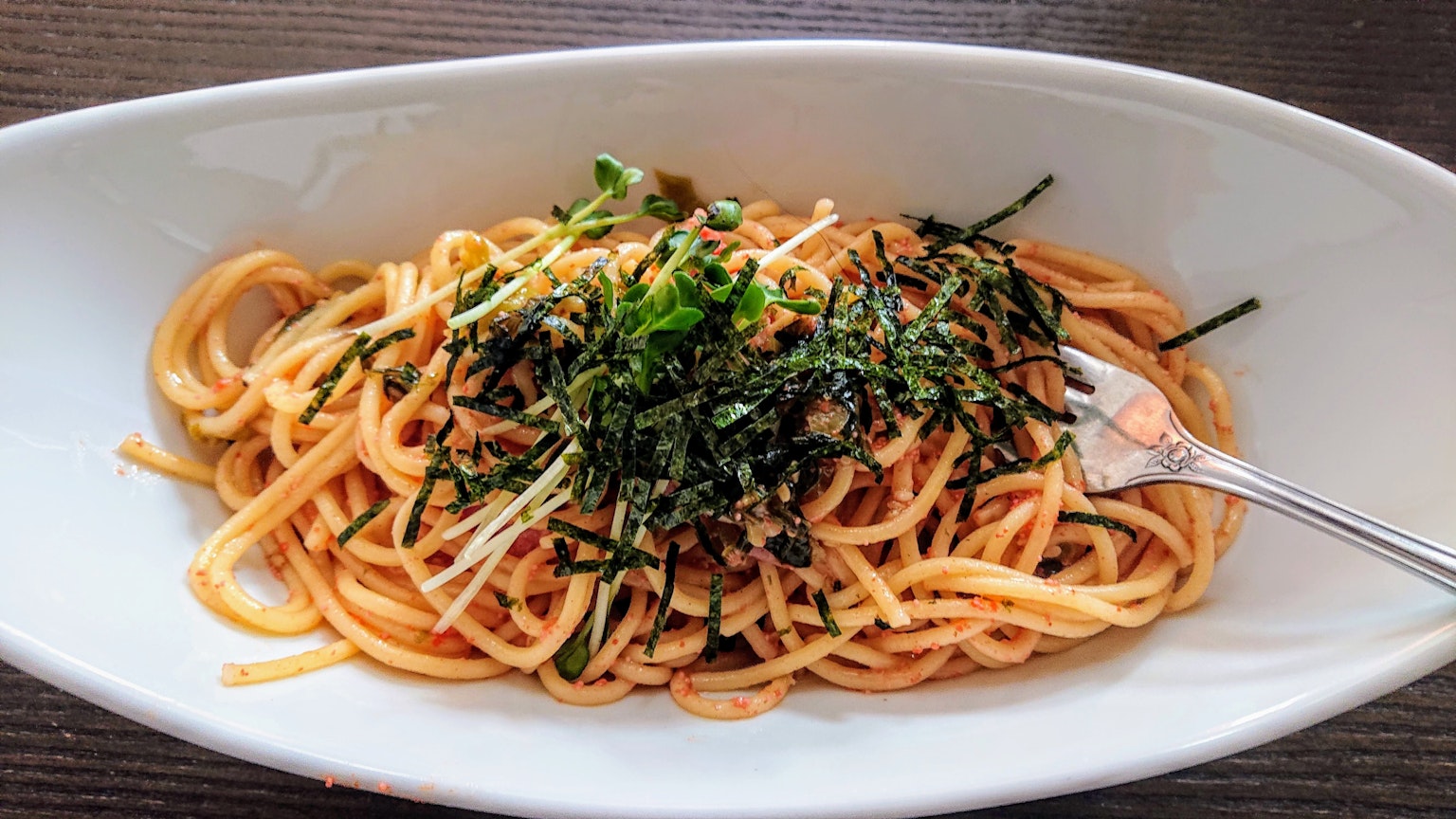 Pasta servita su un piatto bianco guarnita con alga e cipollotto tritato
