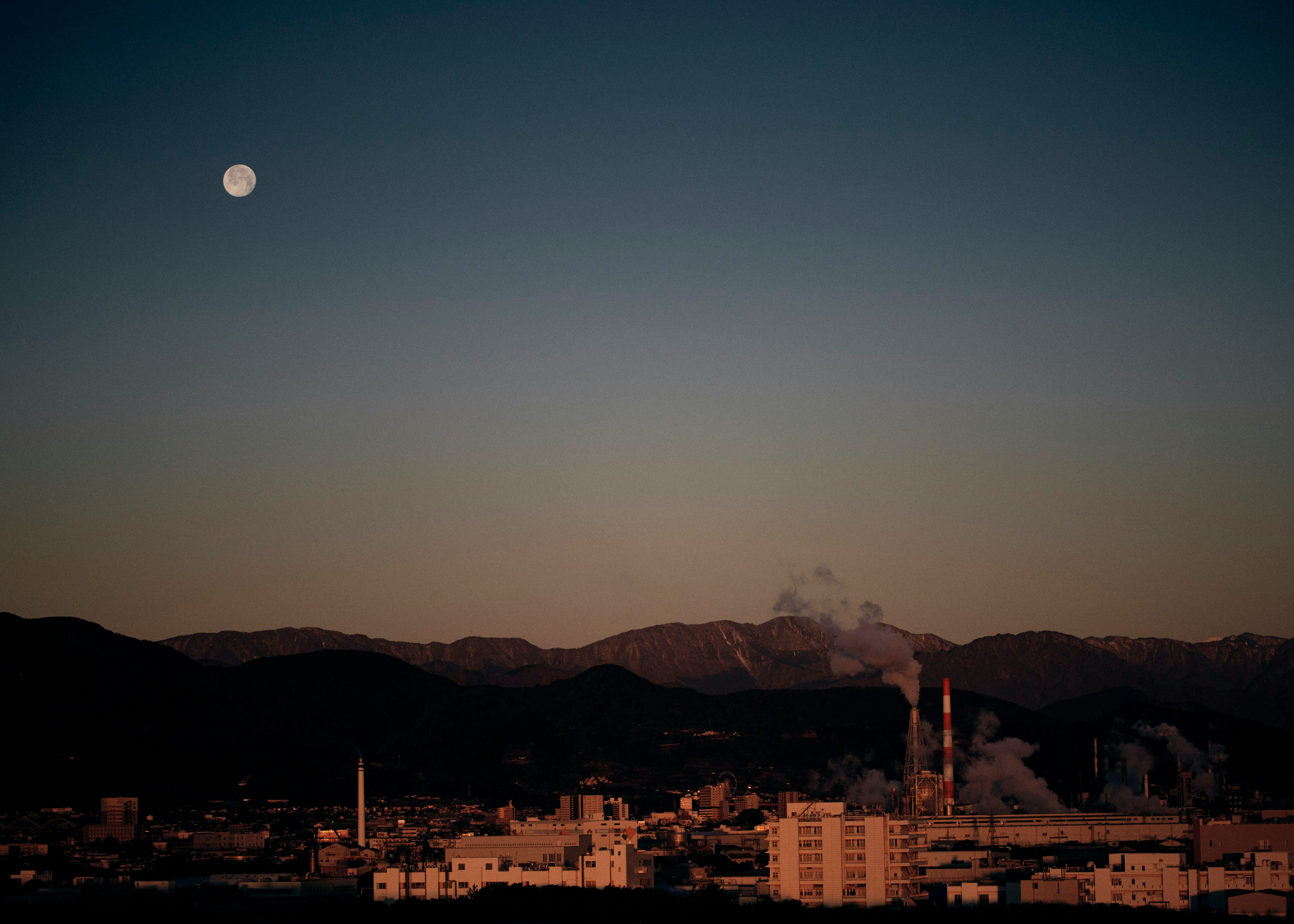 夕暮れの工場群と街並み、月と山並みのシルエット