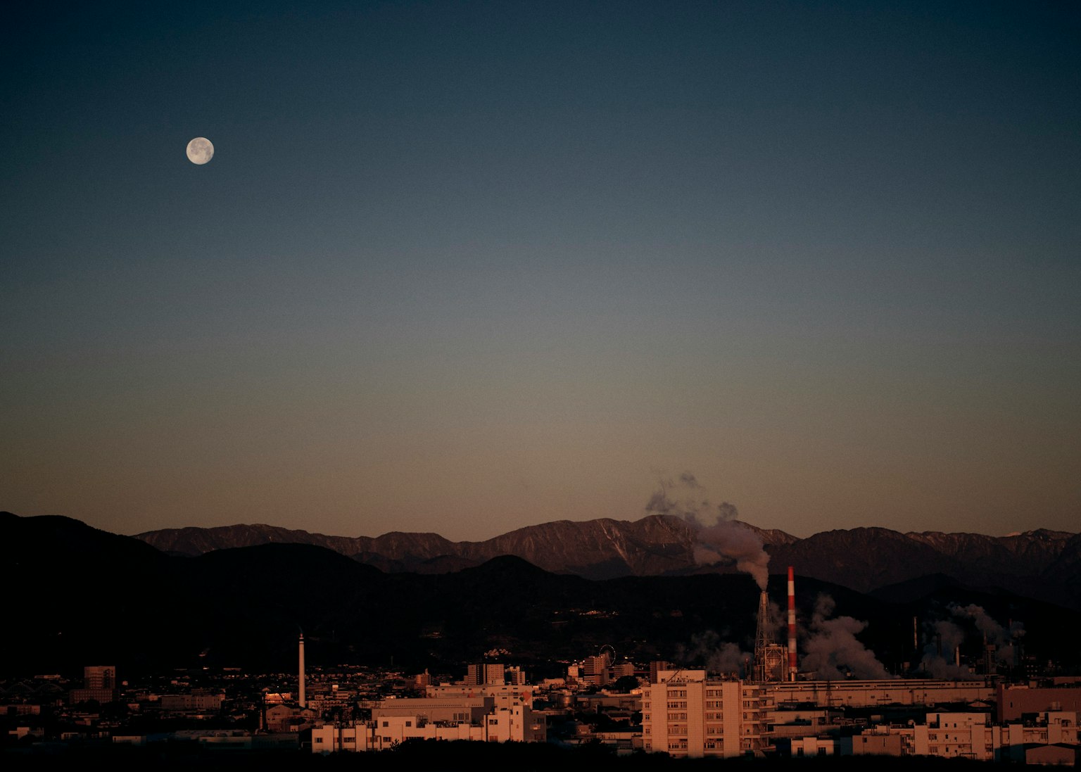 夜空中漂浮的滿月和工廠煙霧背景的山脈